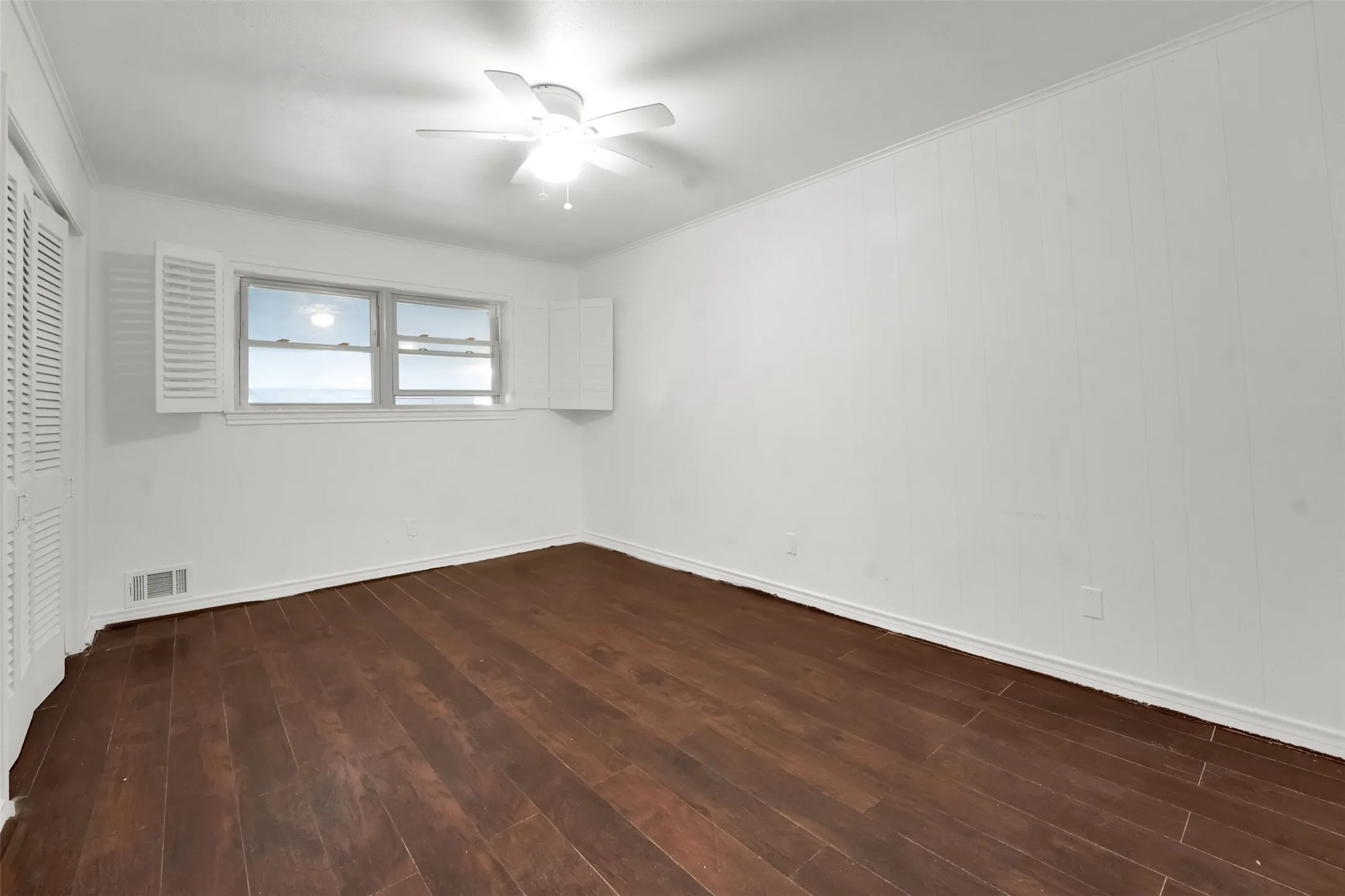 Rich wood-finish flooring, white paneling, white louvered window shutters, and a ceiling fan with light fixture