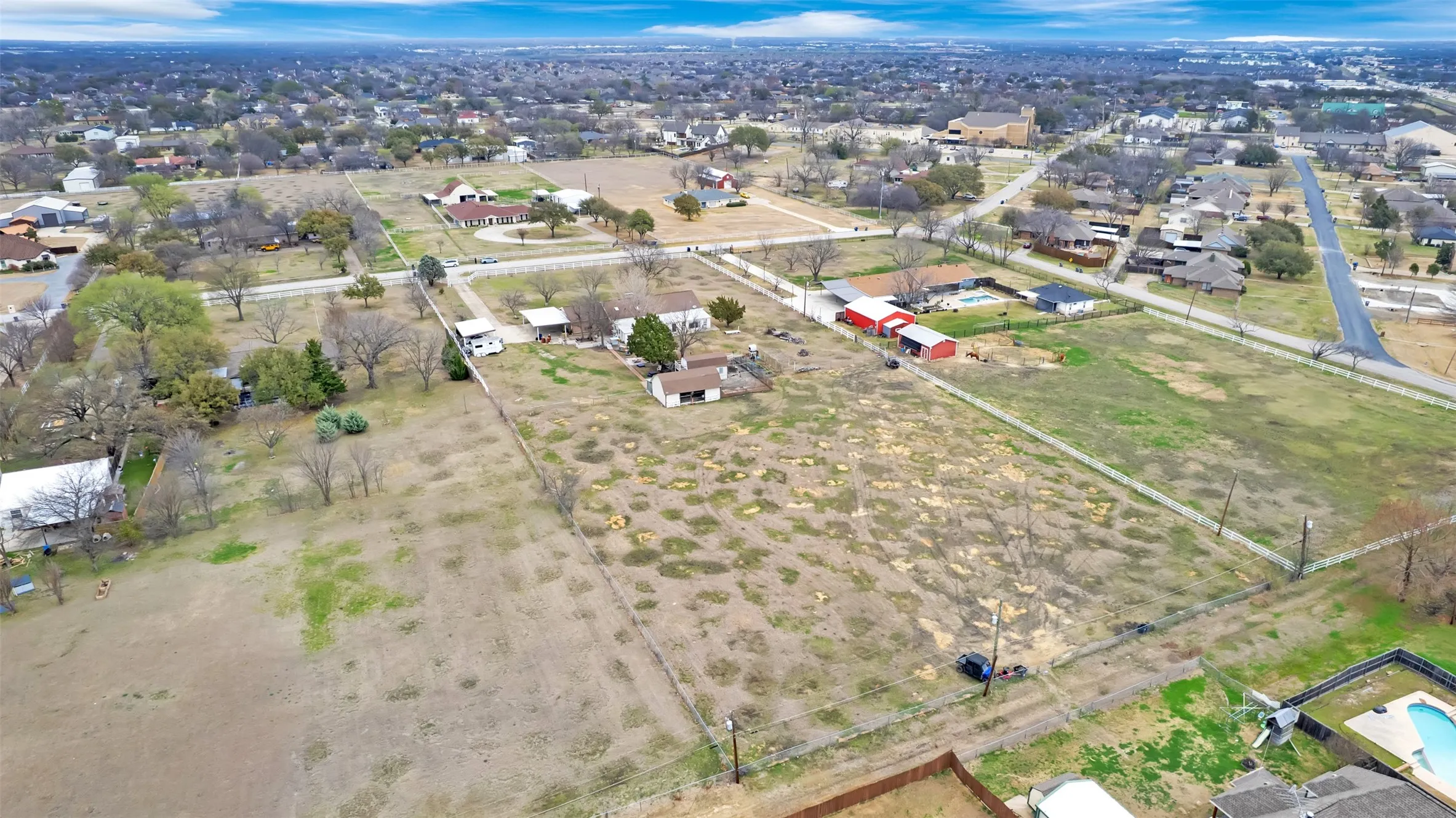 Expansive undeveloped land parcel featuring perimeter fencing, mature trees, and multiple existing structures