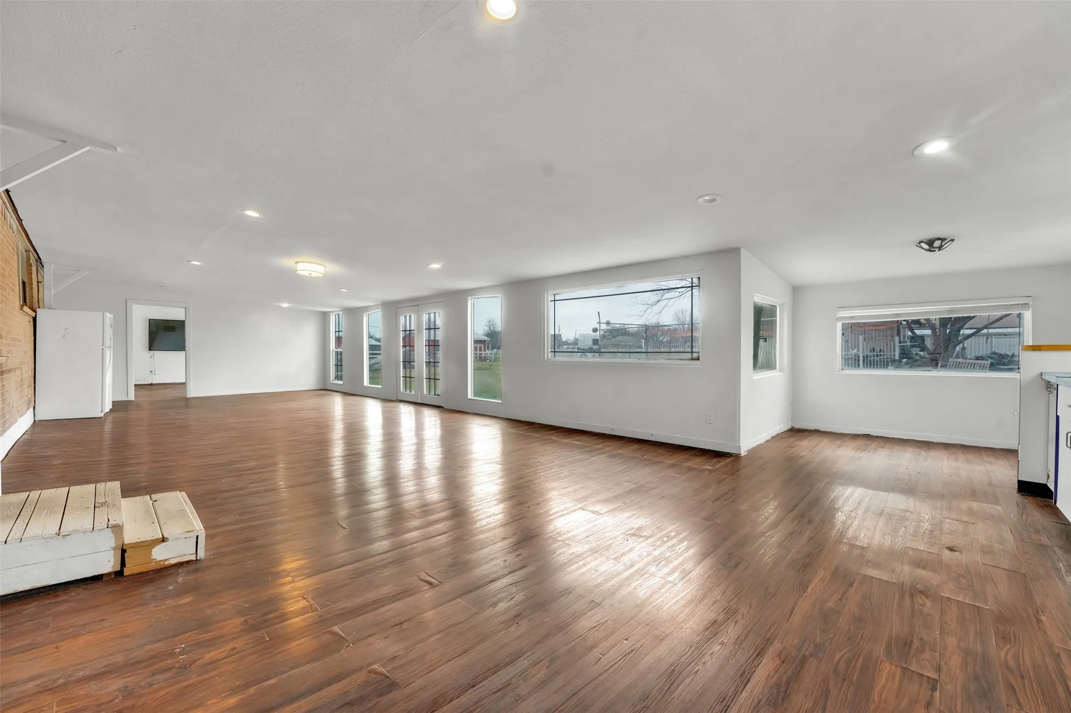 Wood-finish flooring throughout, featuring recessed lighting, multiple large windows, and a partially exposed brick wall