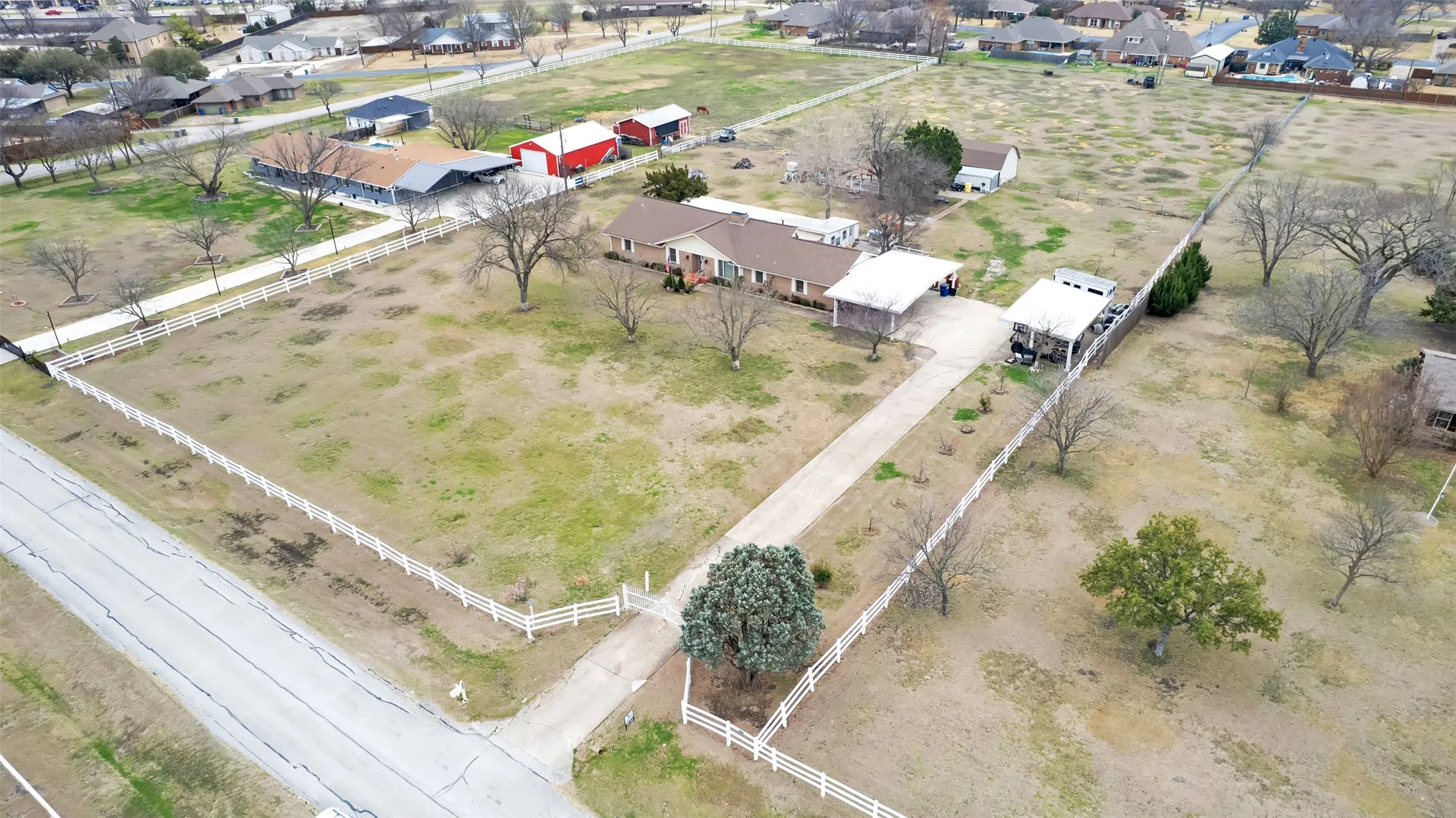 Expansive property featuring a single-story residence, a long private driveway, white picket fencing, mature trees, and a detached red barn