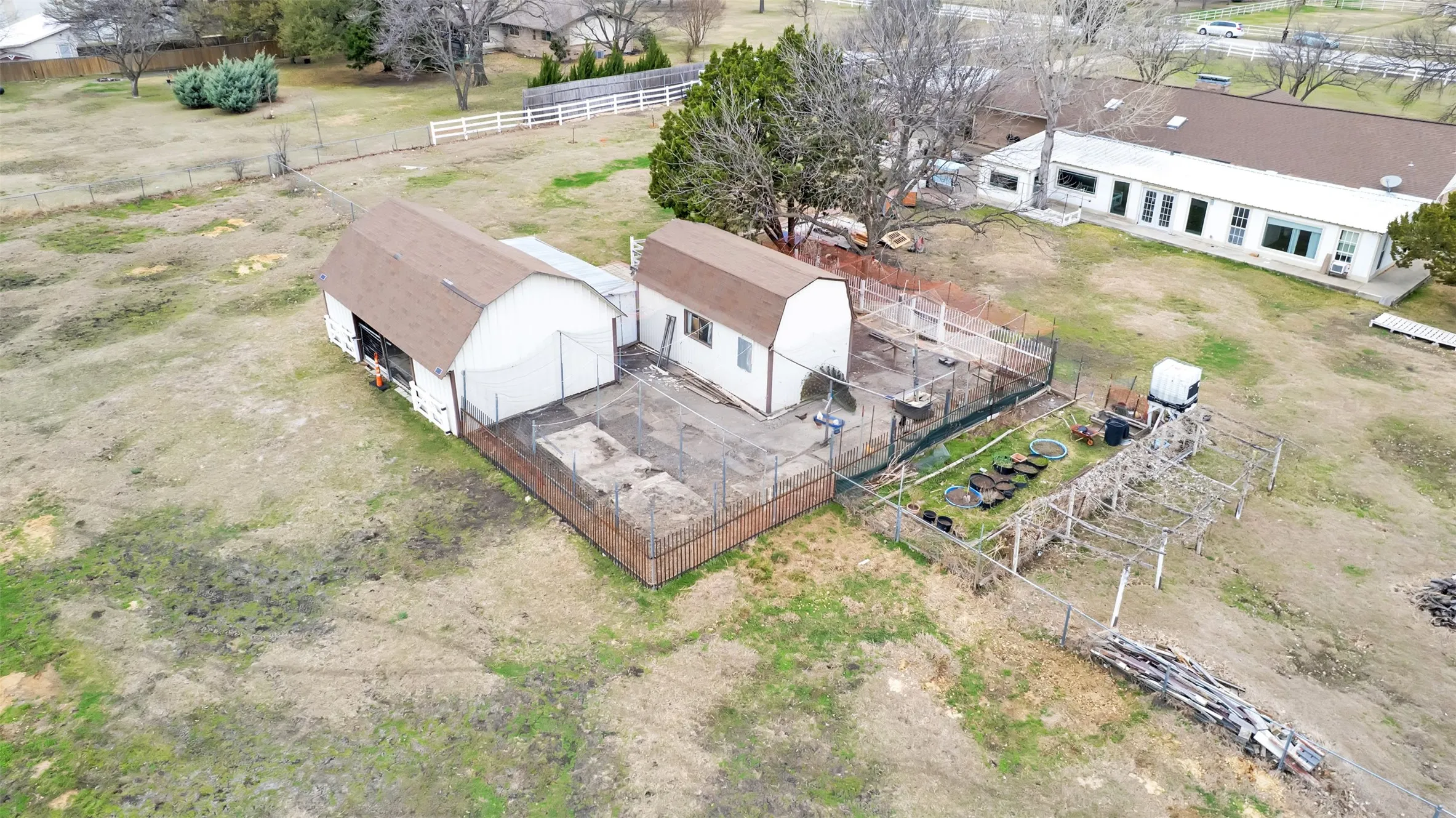 Barn structure with brown shingle roofing, secondary shed with brown shingle roofing, and fenced outdoor enclosures
