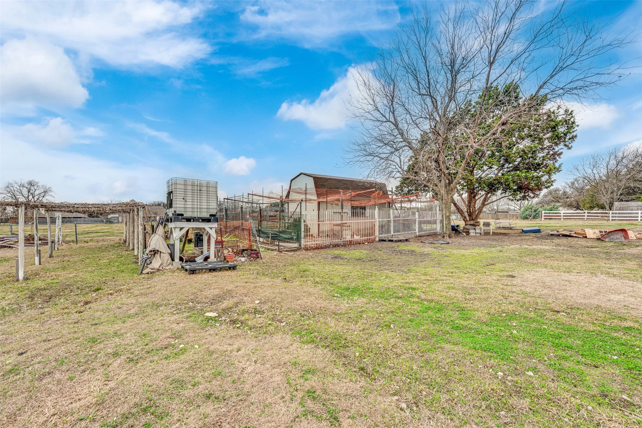 Expansive open land area featuring a large tree, a barn-style structure, and agricultural fencing
