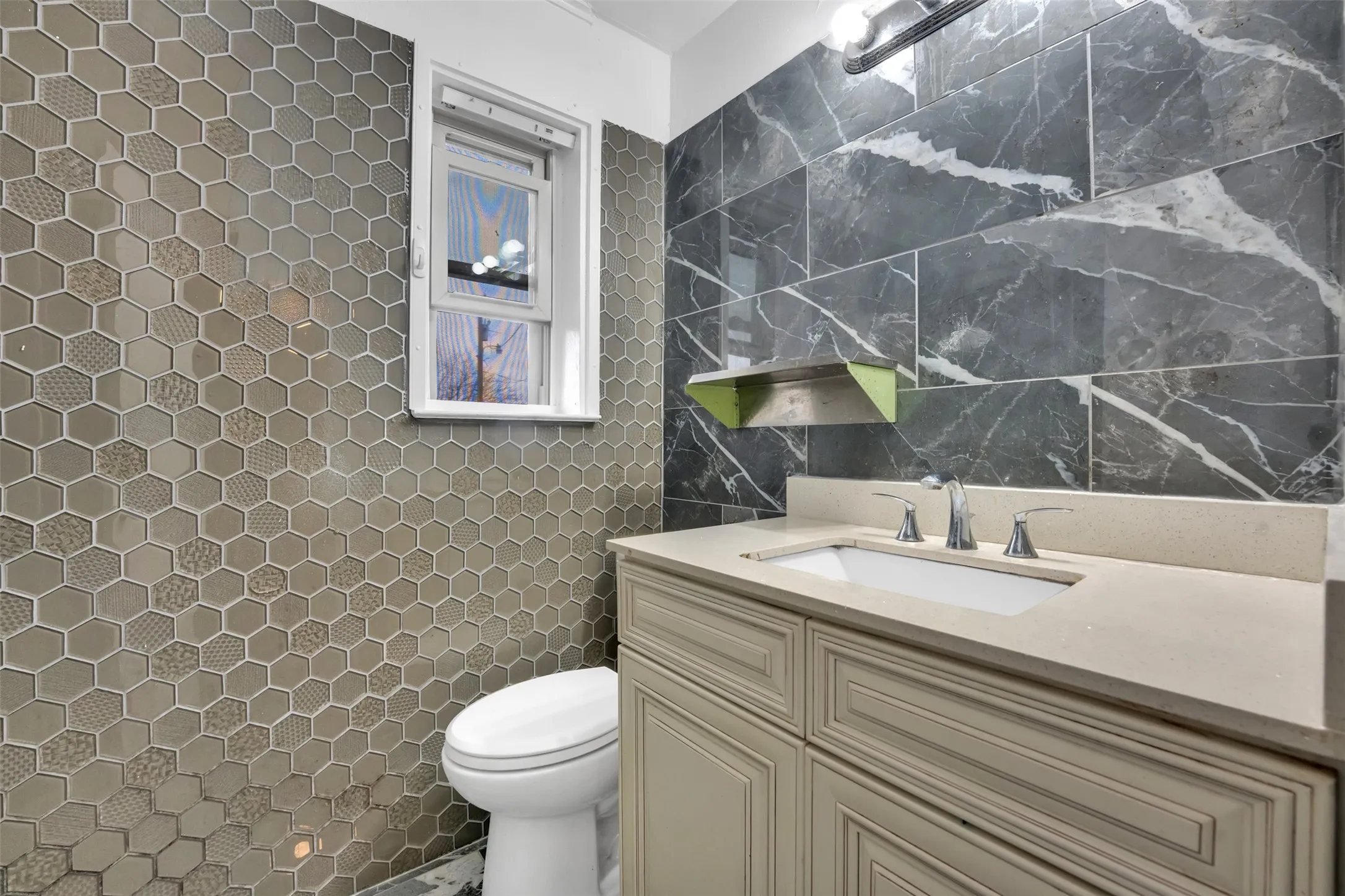 Hexagonal wall tile with varied textures, built-in vanity with light-colored countertop, integrated sink, and wall-mounted lighting
