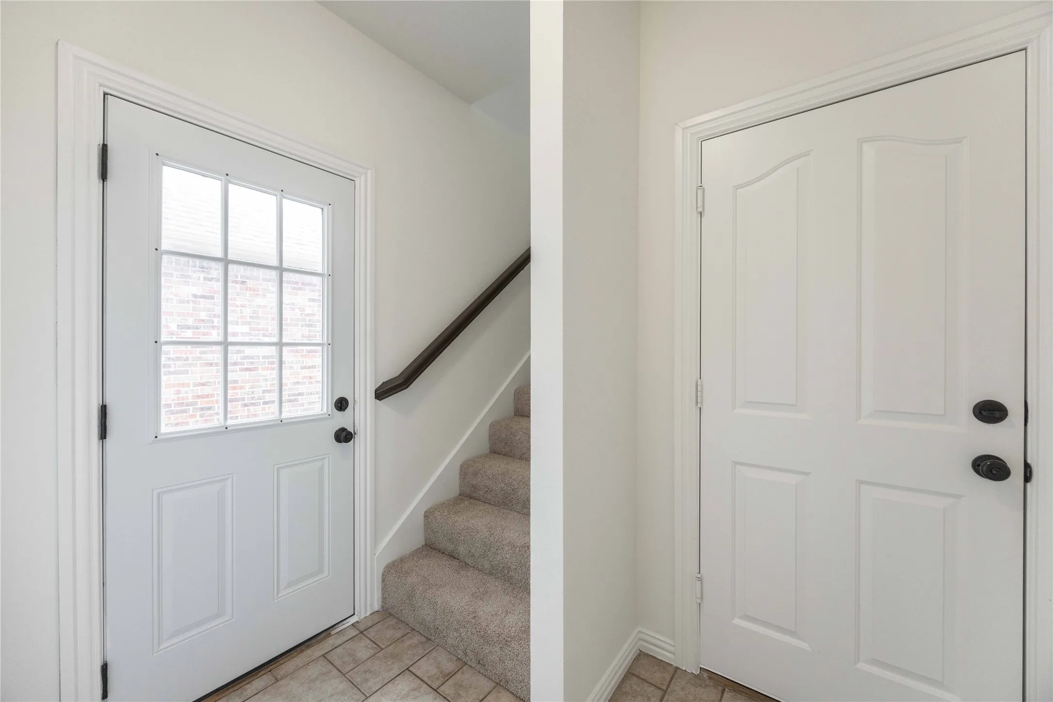 Entryway featuring a paneled door with nine-lite glass, neutral tile flooring, and carpeted stairs with a dark wood handrail