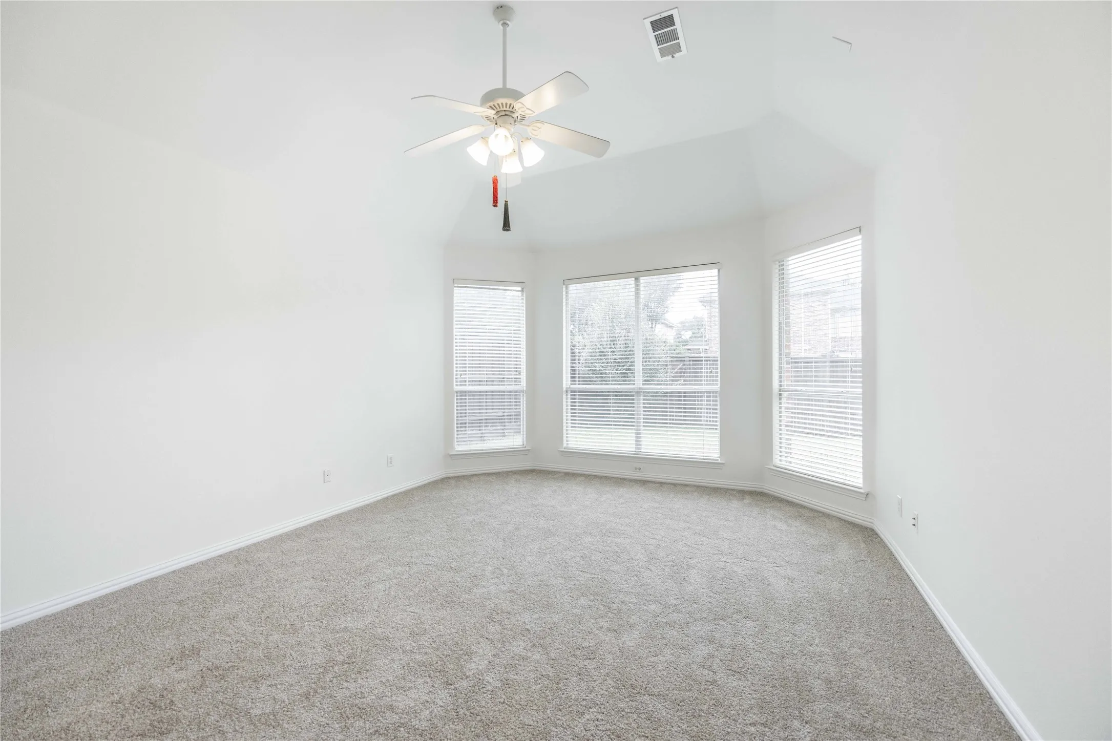 Vaulted ceiling with a ceiling fan, bay window configuration, multiple windows with blinds, and light-toned carpeting