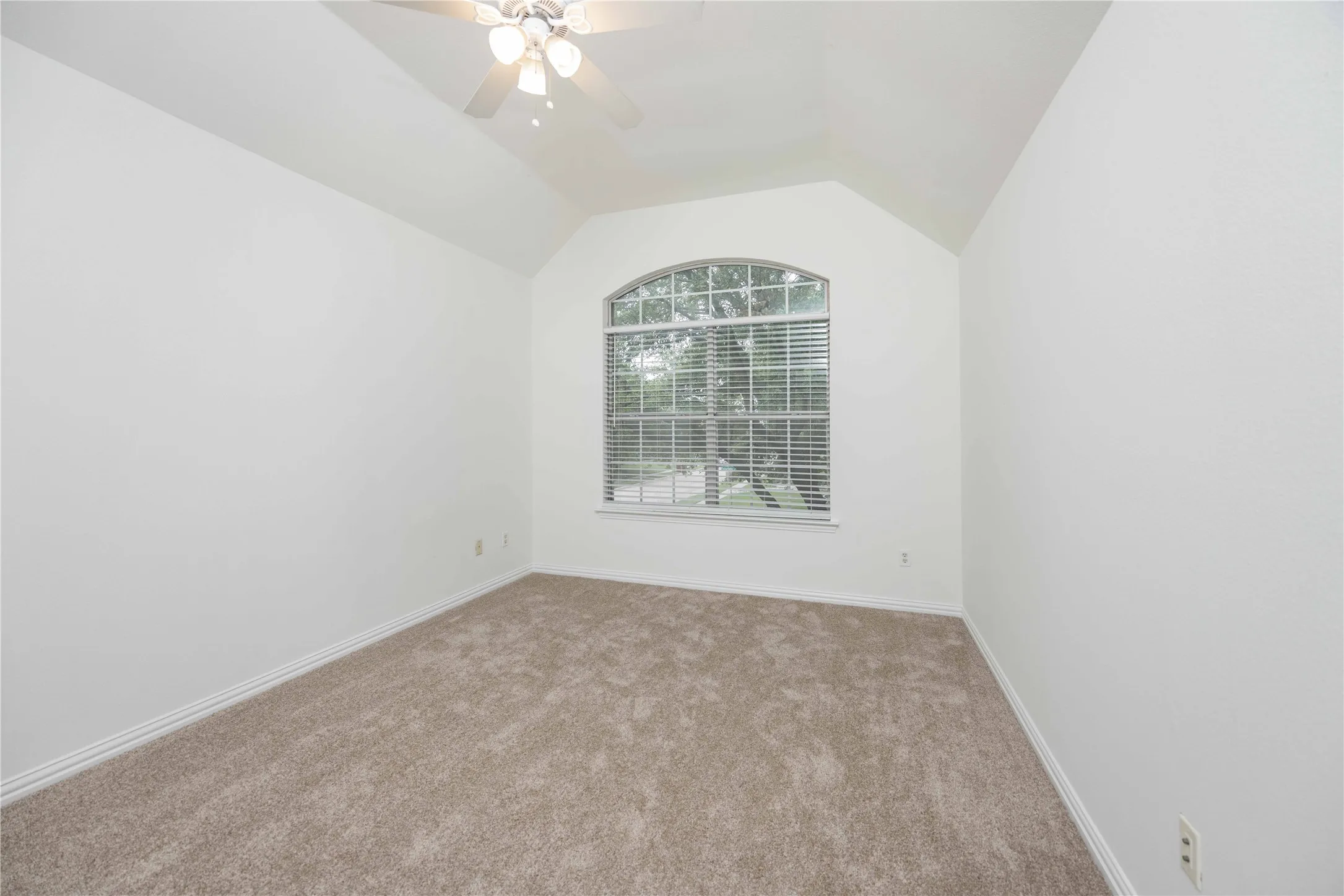 Vaulted ceiling with an installed ceiling fan, an arched window, and carpet flooring