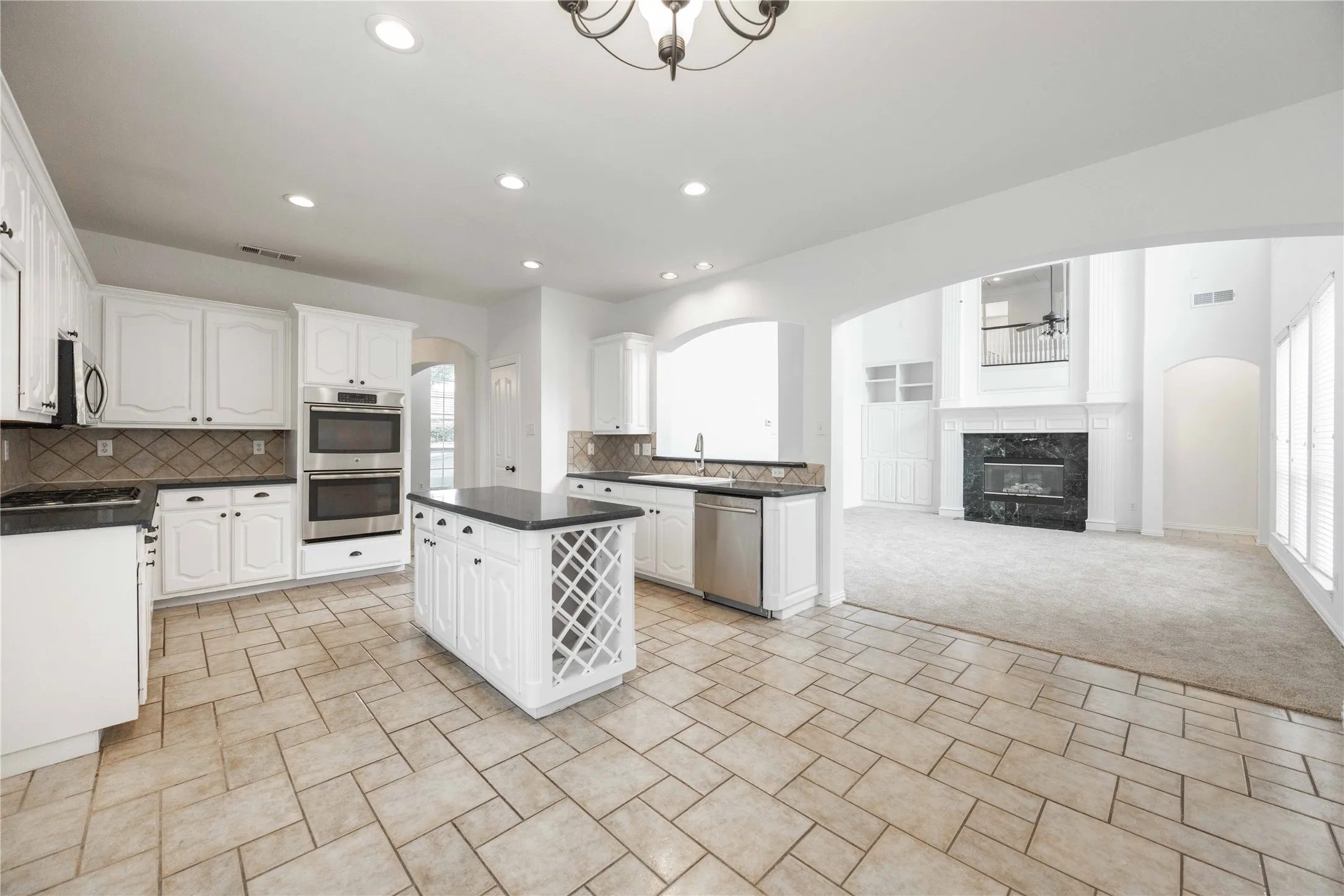 Kitchen featuring white cabinetry, dark countertops, a double wall oven, a center island with built-in wine storage, and tile flooring