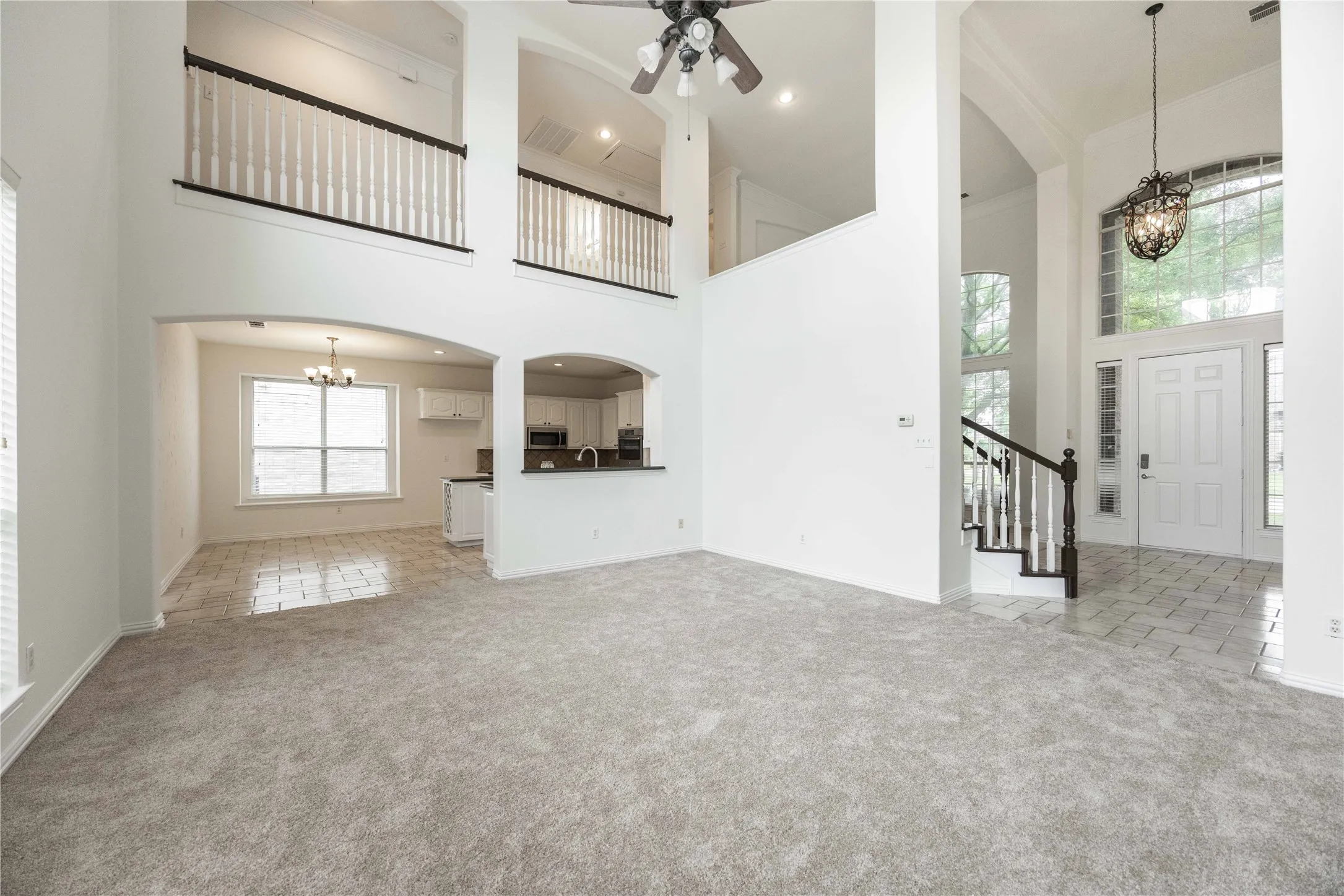Two-story ceiling, arched doorways, white interior paint, wood-finish staircase with white balusters, and a decorative chandelier