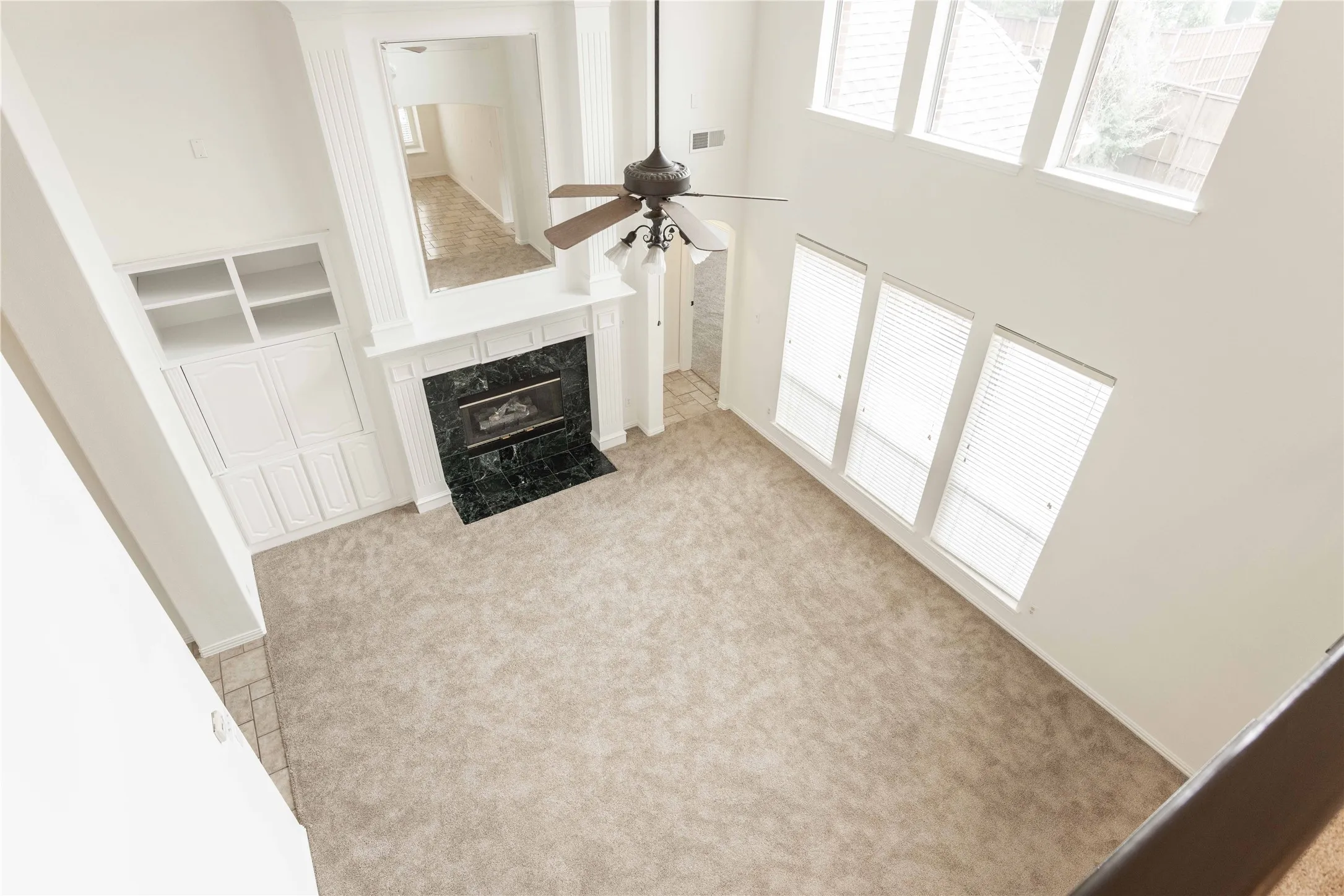 Two-story living area featuring a ceiling fan, fireplace with dark stone surround, white mantel, and built-in white cabinetry