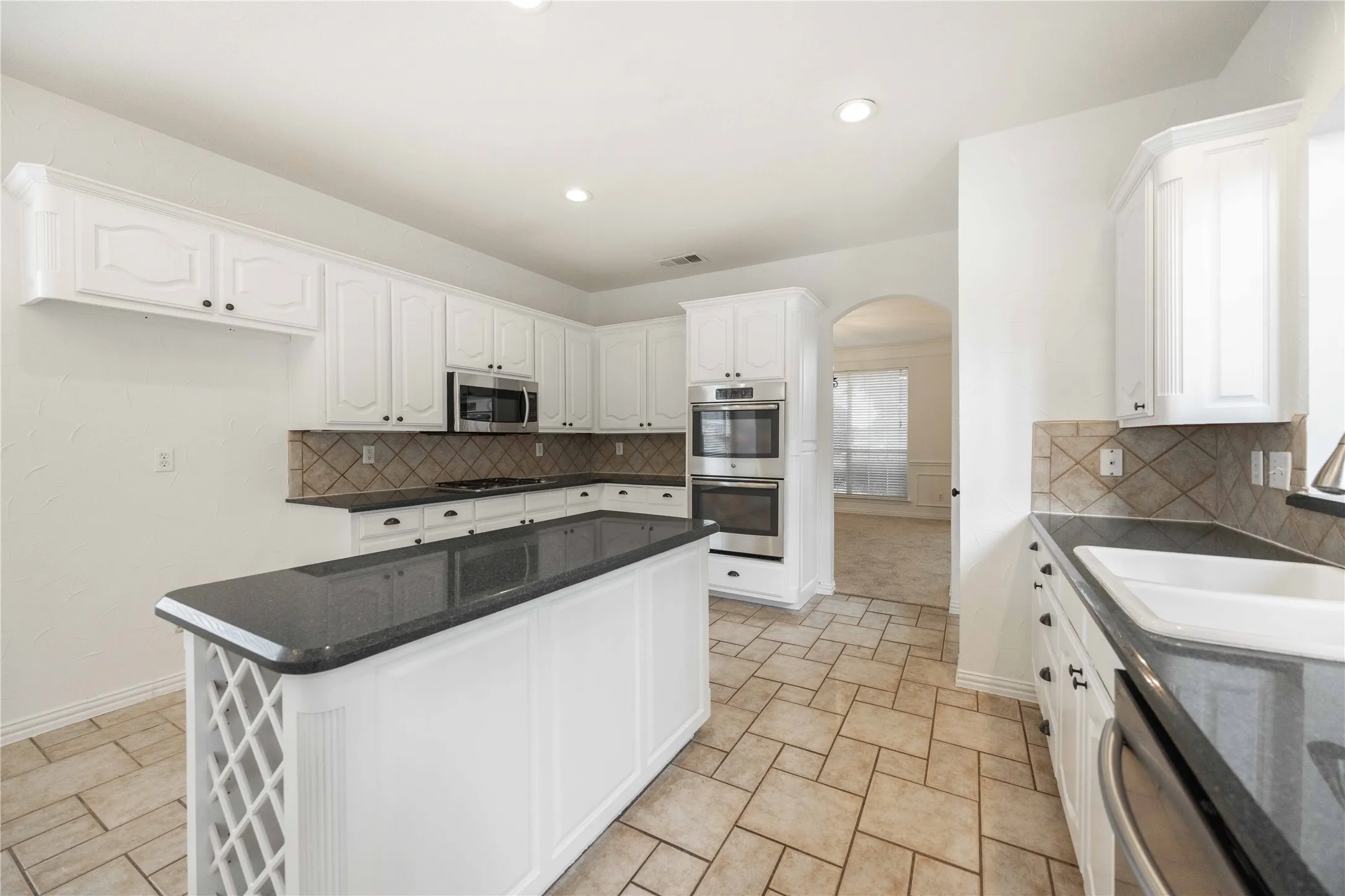 White cabinetry with dark hardware, stone-finish countertops, stainless steel appliances, tiled backsplash, and tiled flooring