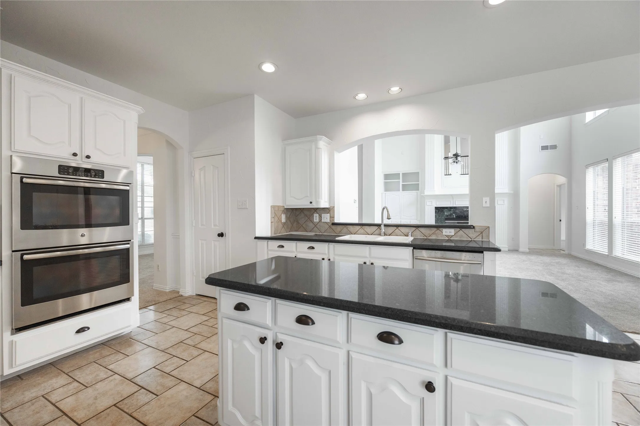 Kitchen featuring white cabinetry, stainless steel double ovens, a center island with a dark countertop, and tiled flooring