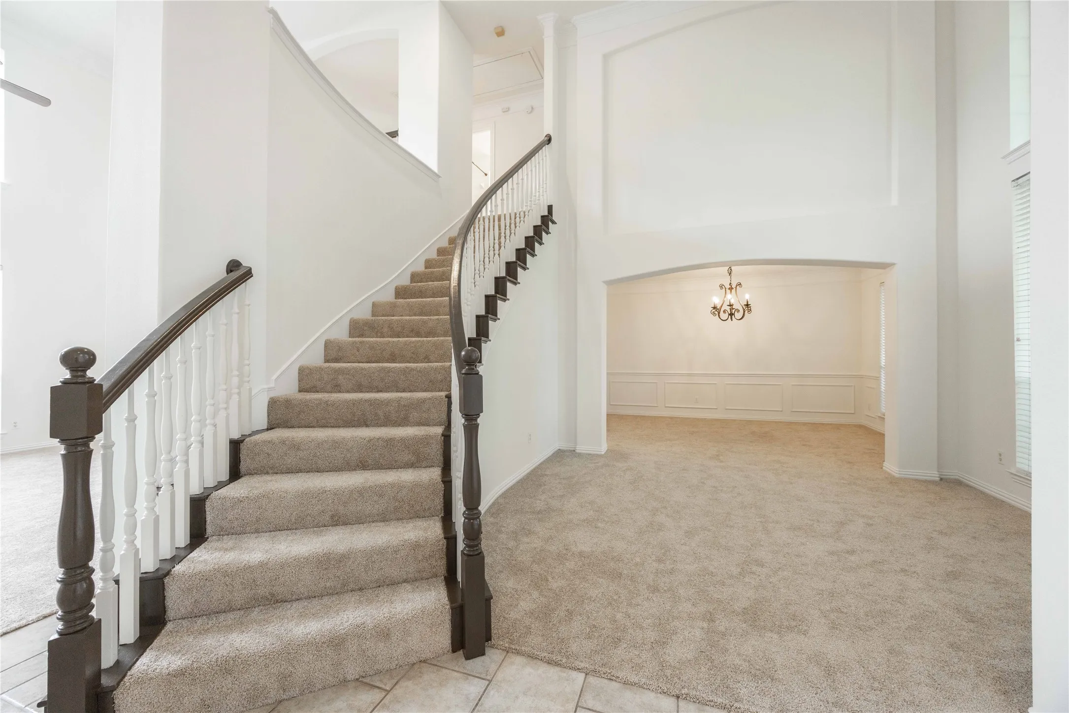 Curved staircase with wood newel posts and balusters, carpeted treads, and tiled entry