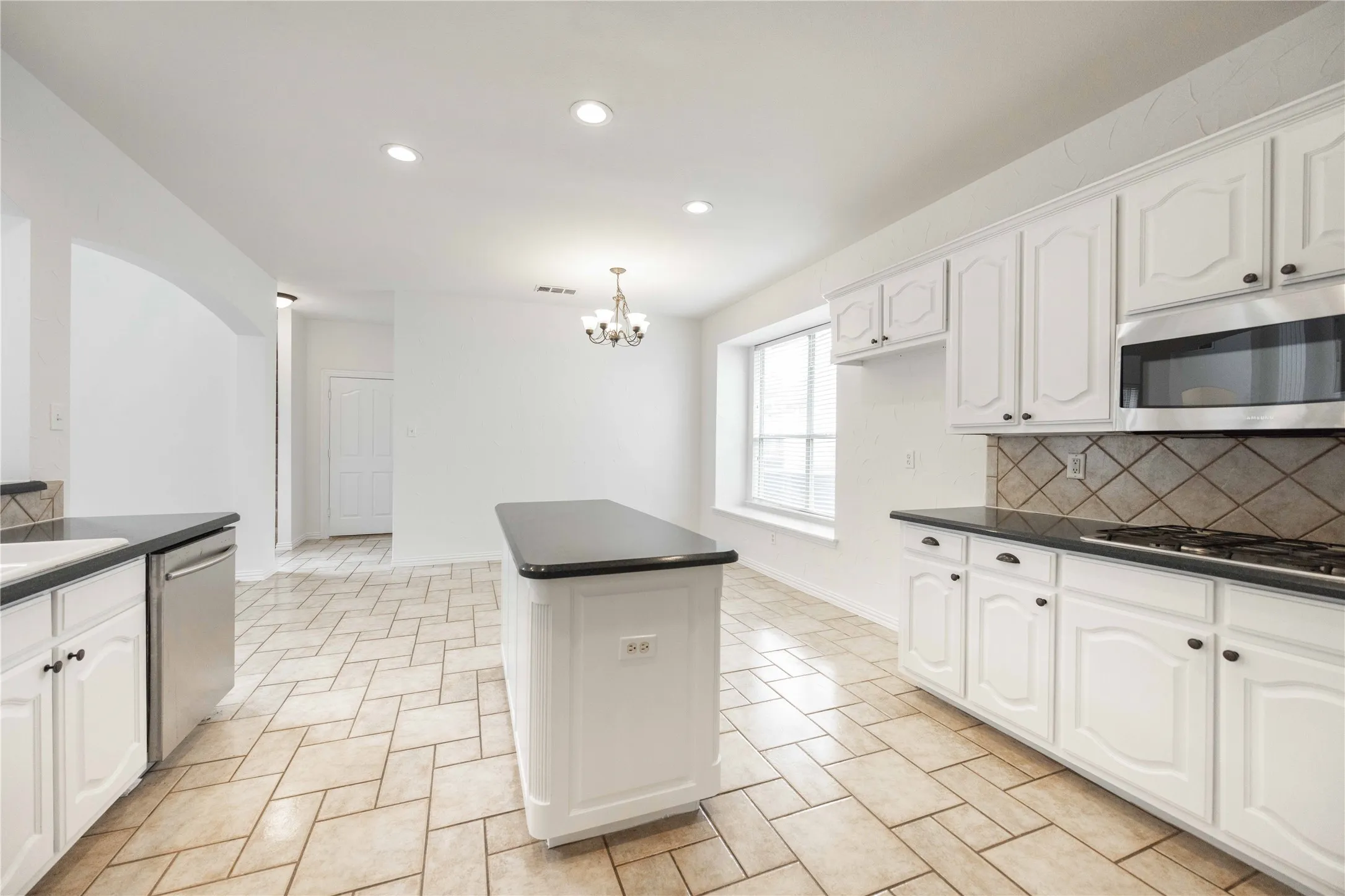 Kitchen featuring white cabinetry, dark countertops, a tile backsplash, stainless steel appliances, and a central island