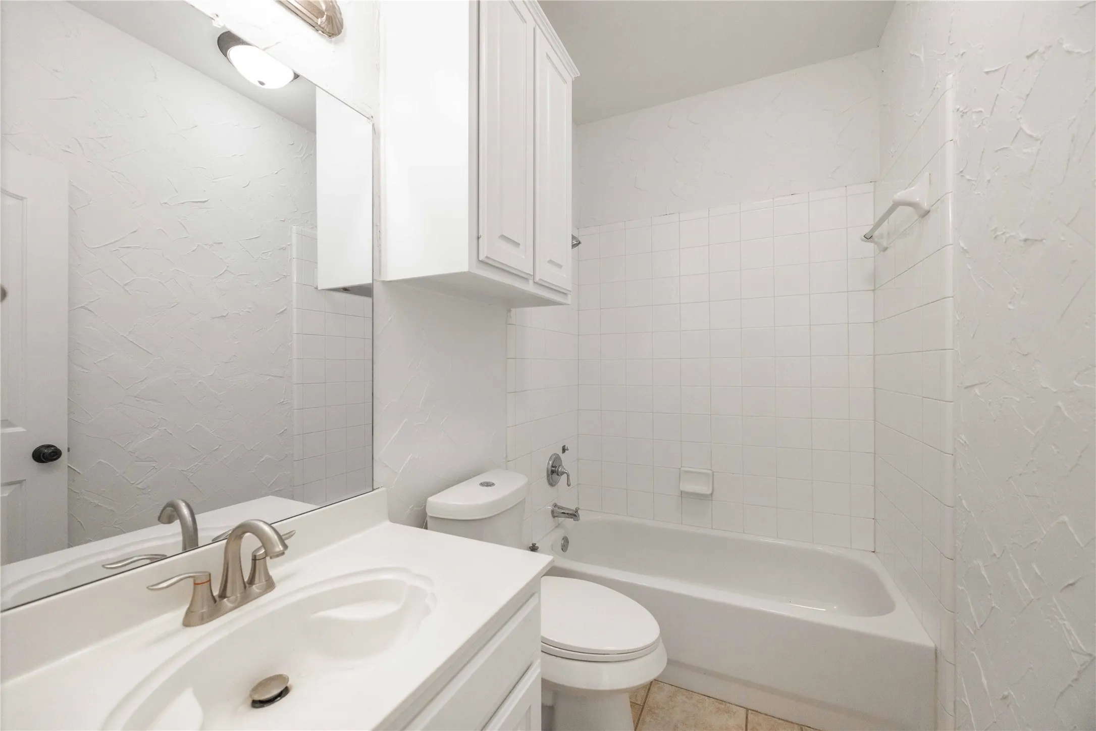 White vanity with integrated sink, brushed nickel faucet, wall-mounted mirror, white shaker-style cabinetry, and a full bathtub with white subway tile surround