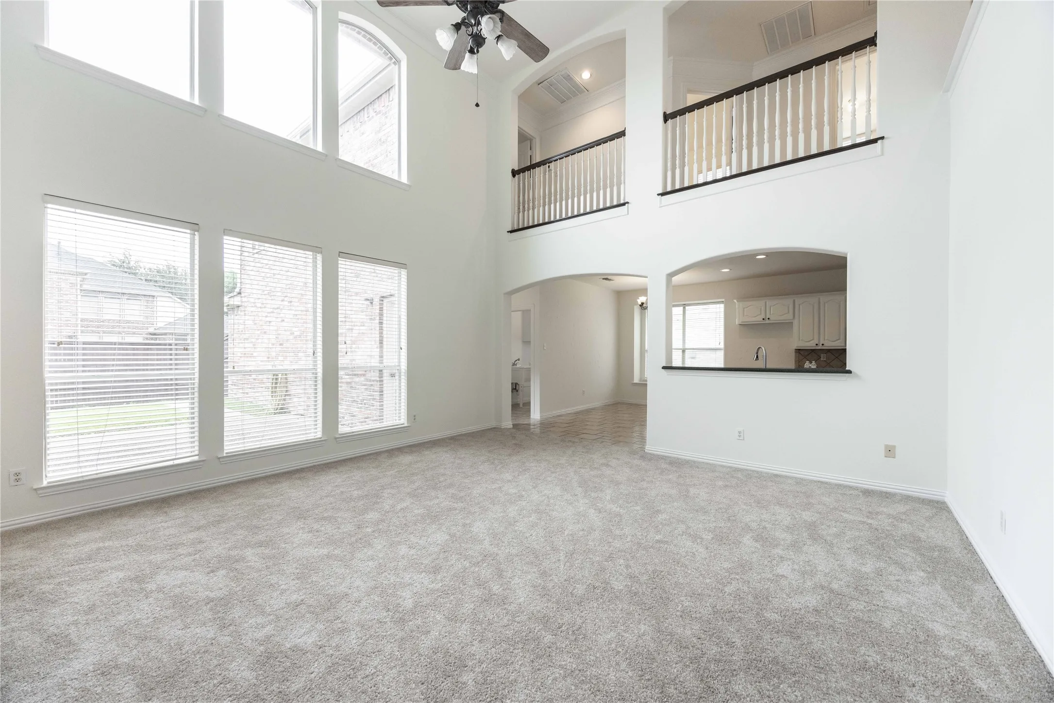 Two-story living area with high ceilings, upper-level windows, and an arched pass-through to the kitchen
