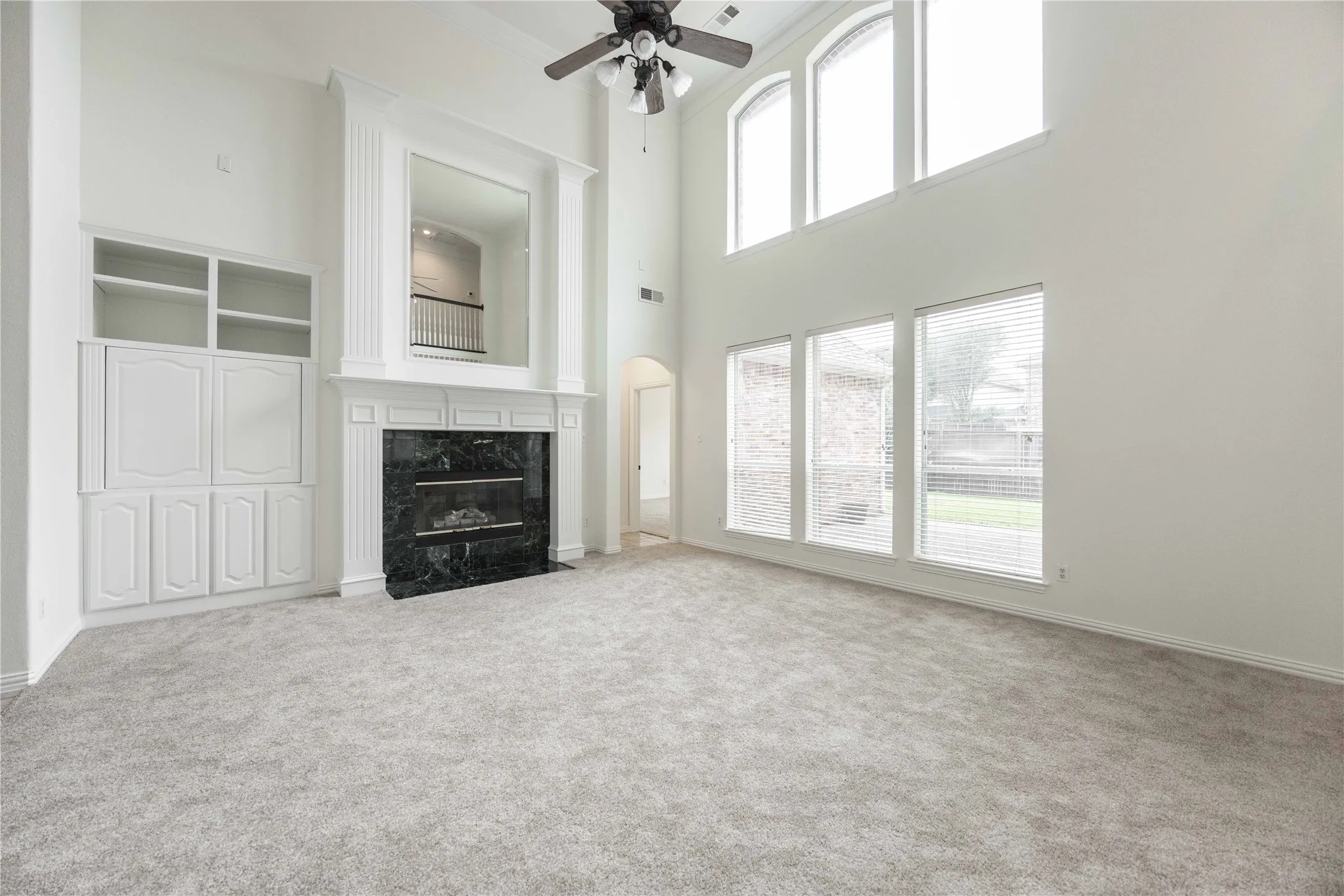 Two-story living area with high ceilings, a built-in media cabinet, a fireplace with a dark stone surround, and multiple windows
