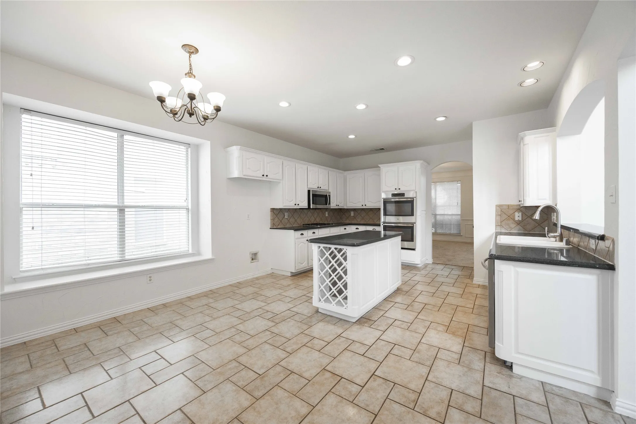 Kitchen featuring white cabinetry, dark countertops, a central island with wine storage, recessed lighting, and a chandelier