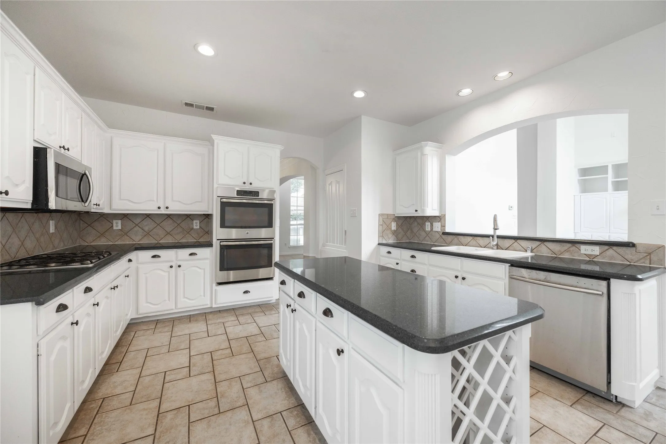 White cabinetry with black hardware, dark countertops, a stainless steel double oven, and tiled flooring