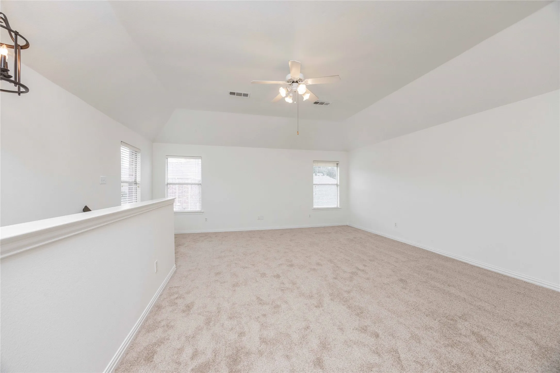 Spacious room featuring vaulted ceilings, neutral carpeting, two windows, and a ceiling fan