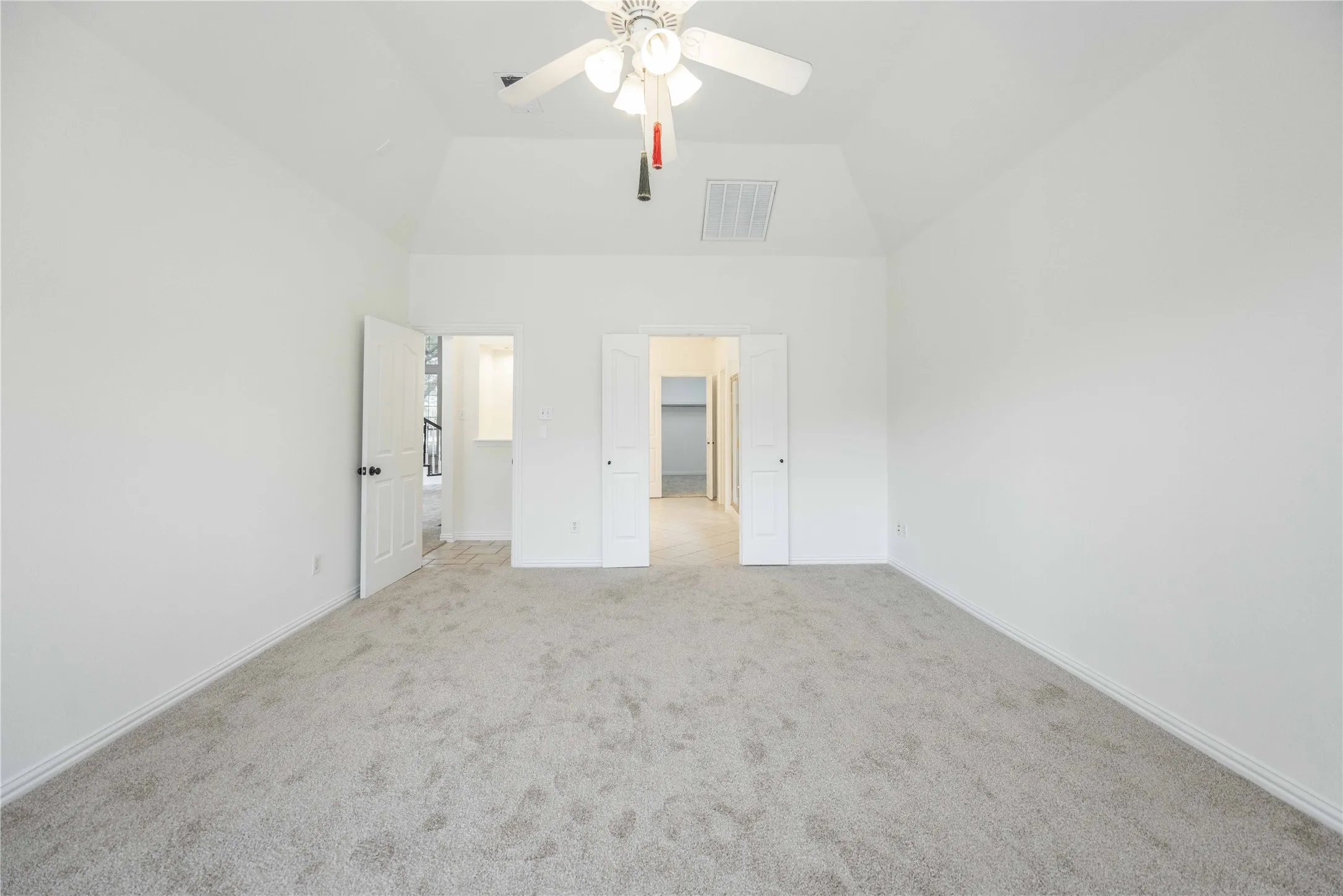 Vaulted ceiling, light-toned carpet, white walls, ceiling fan with light fixture, and white interior doors