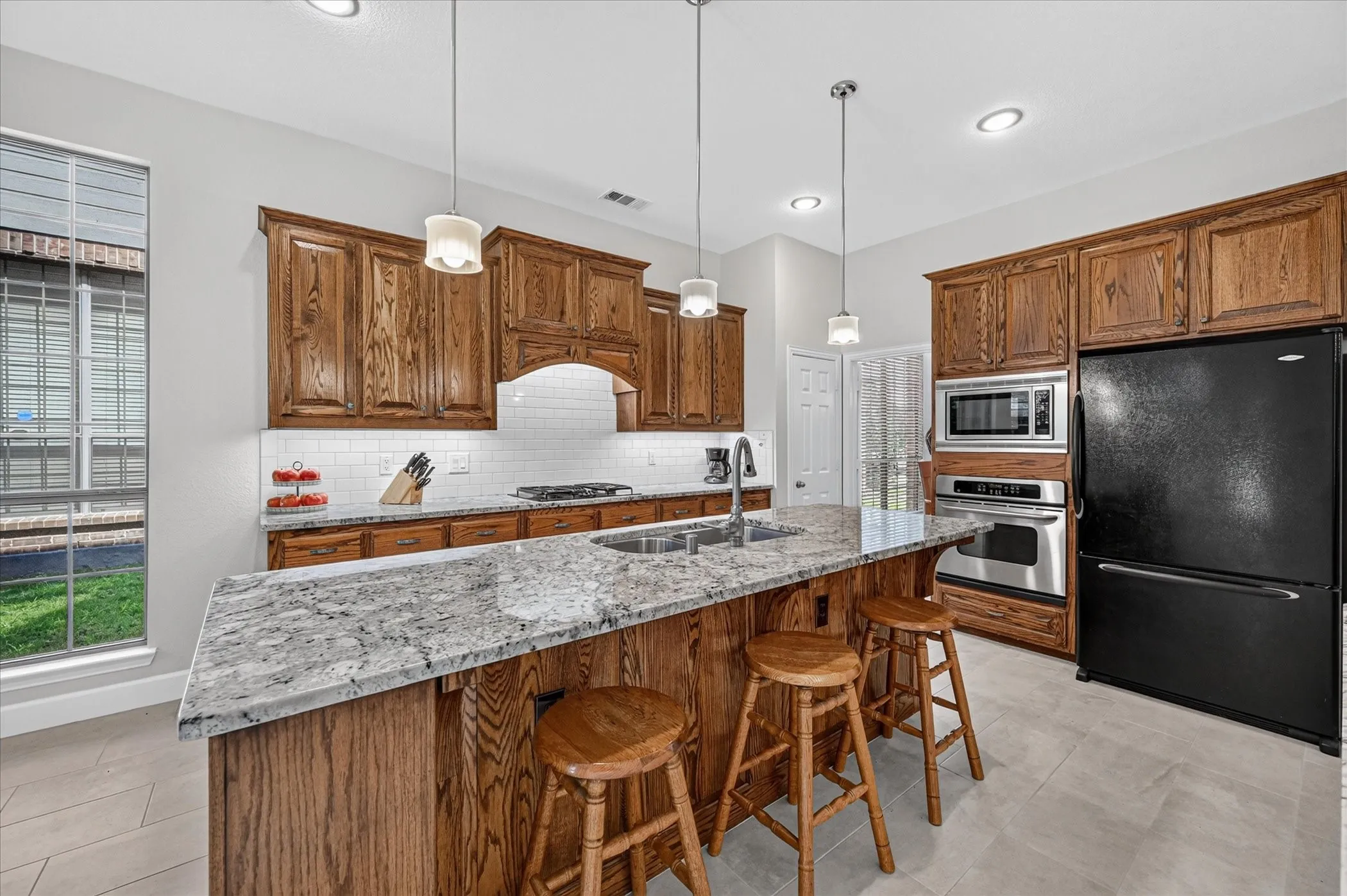 The kitchen features a stainless steel microwave and wall oven, undermount sink, and gas stove. There's also a custom bookcase