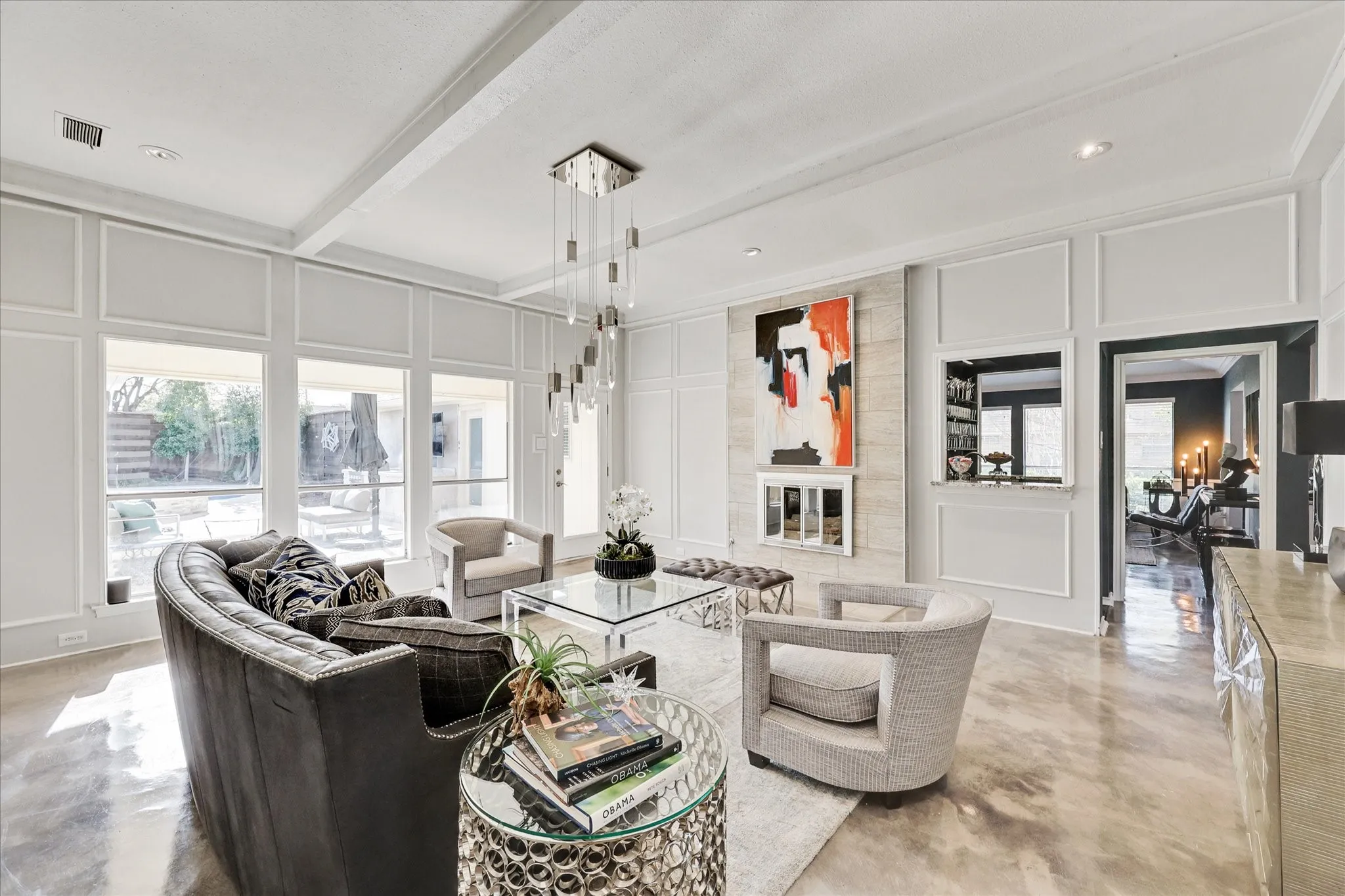 Exposed ceiling beams, integrated shelving with accent lighting, large glass door, multiple large windows, and a multi-tiered chandelier
