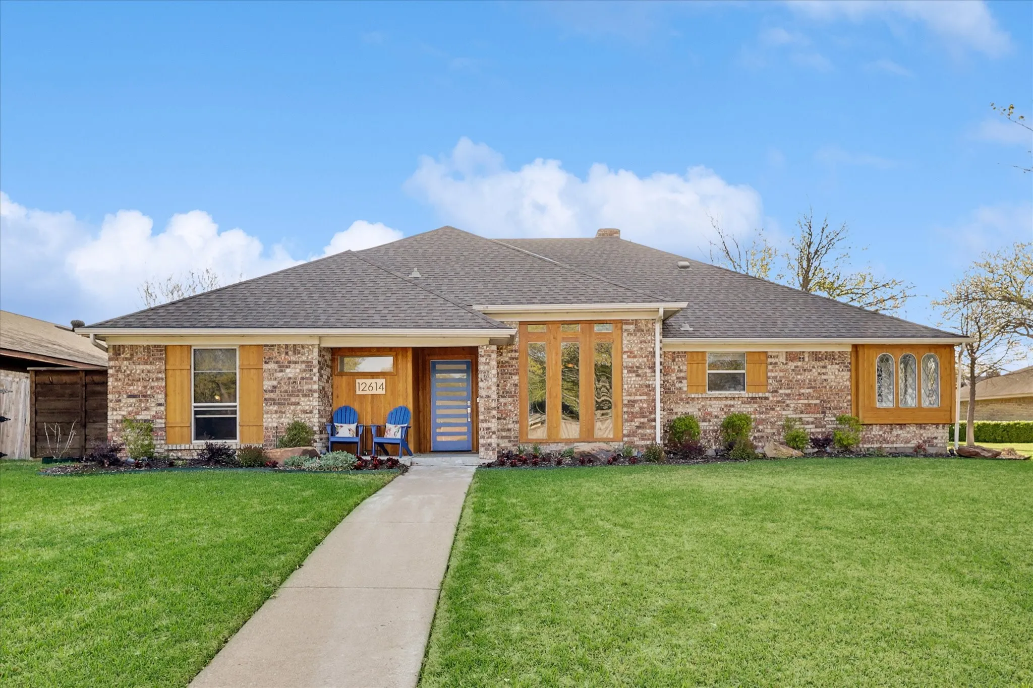 Brick exterior with a dark shingle roof, wood-finish window accents, and a light blue entry door