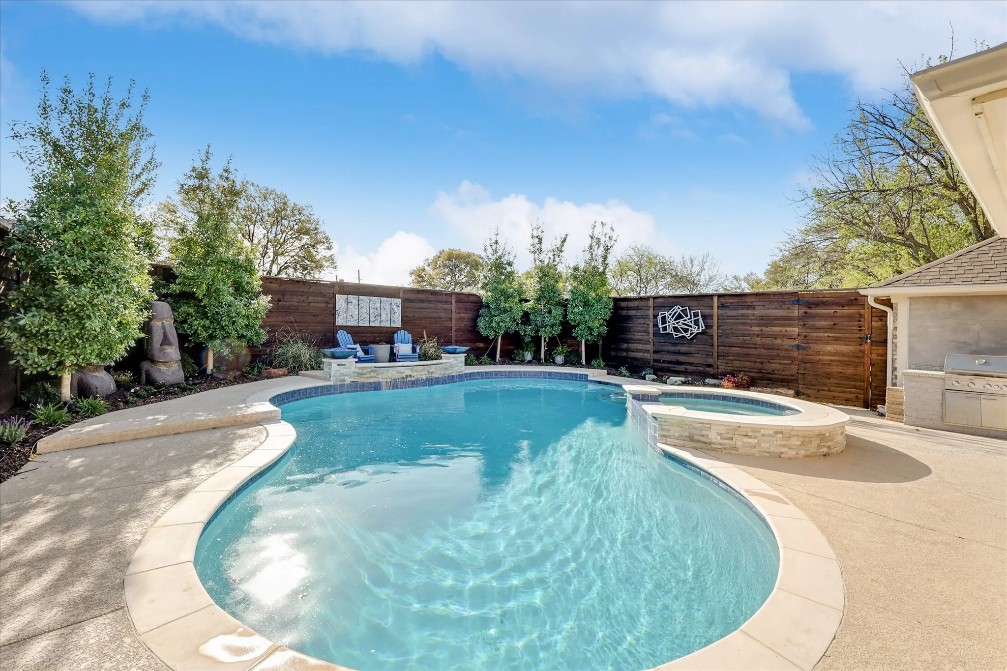 Freeform swimming pool with integrated spa and stone surround, surrounded by concrete decking and a wood privacy fence