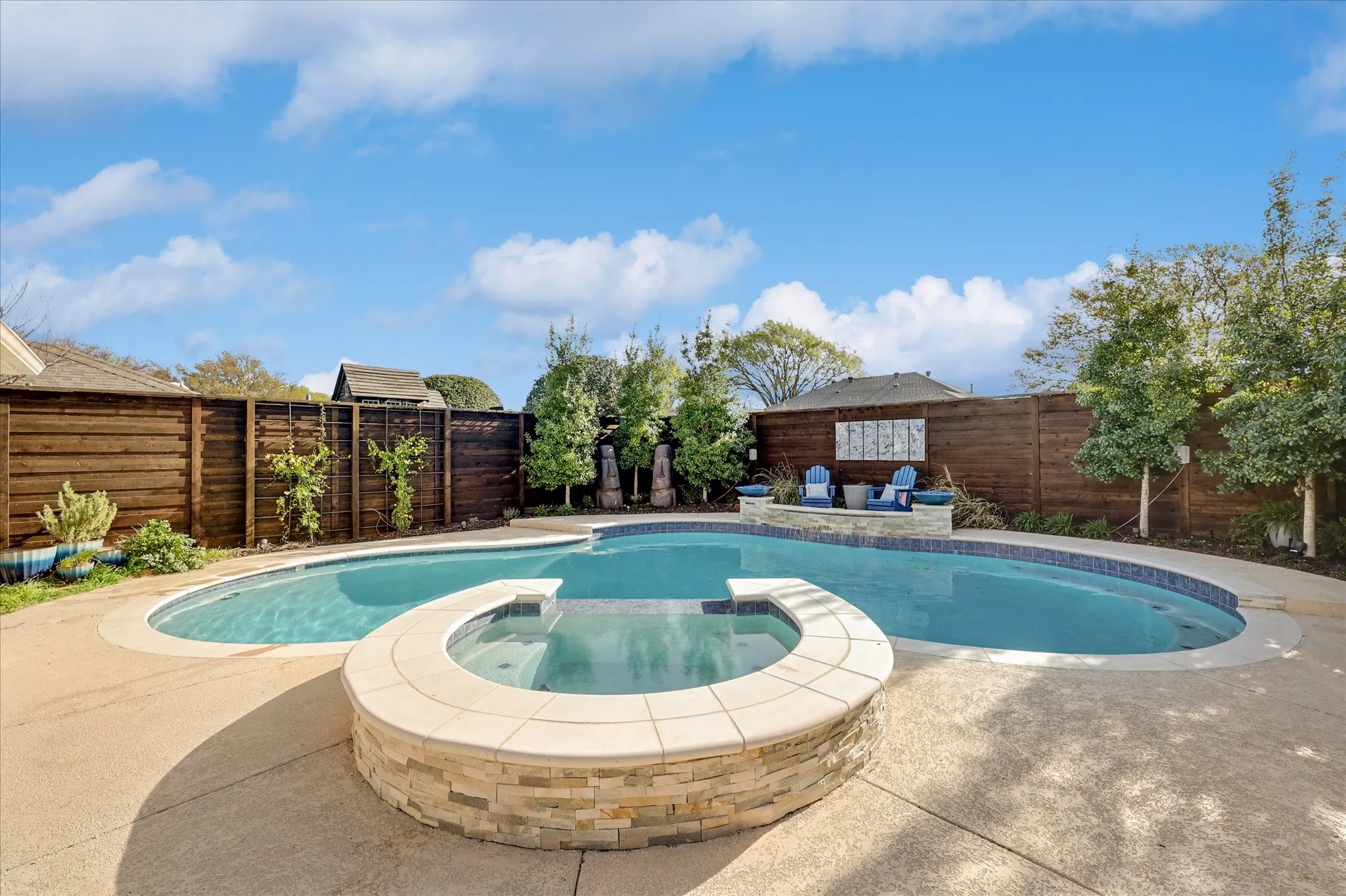 Custom-shaped swimming pool with an integrated spa, surrounded by concrete decking and mature landscaping