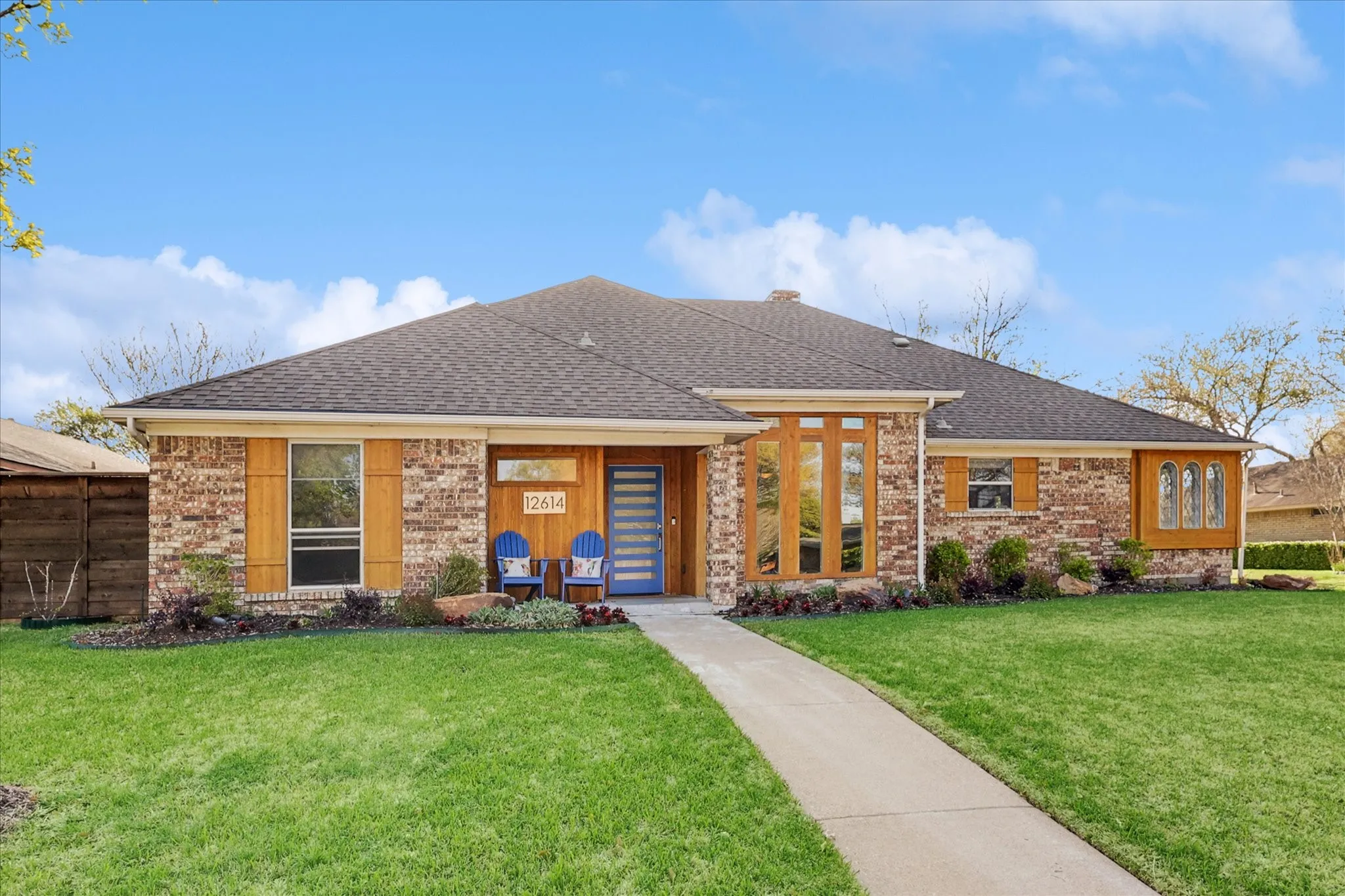 Brick exterior with wood-finish accents, a dark shingle roof, and a prominent blue entry door