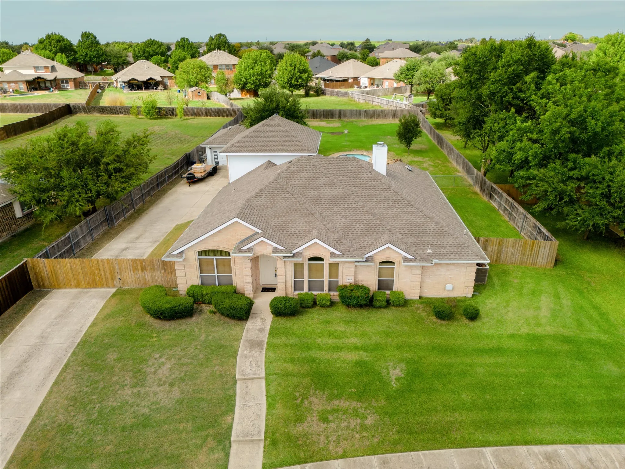 Single-story brick exterior residence featuring a composite shingle roof, arched windows, an attached garage, and an expansive fenced backyard