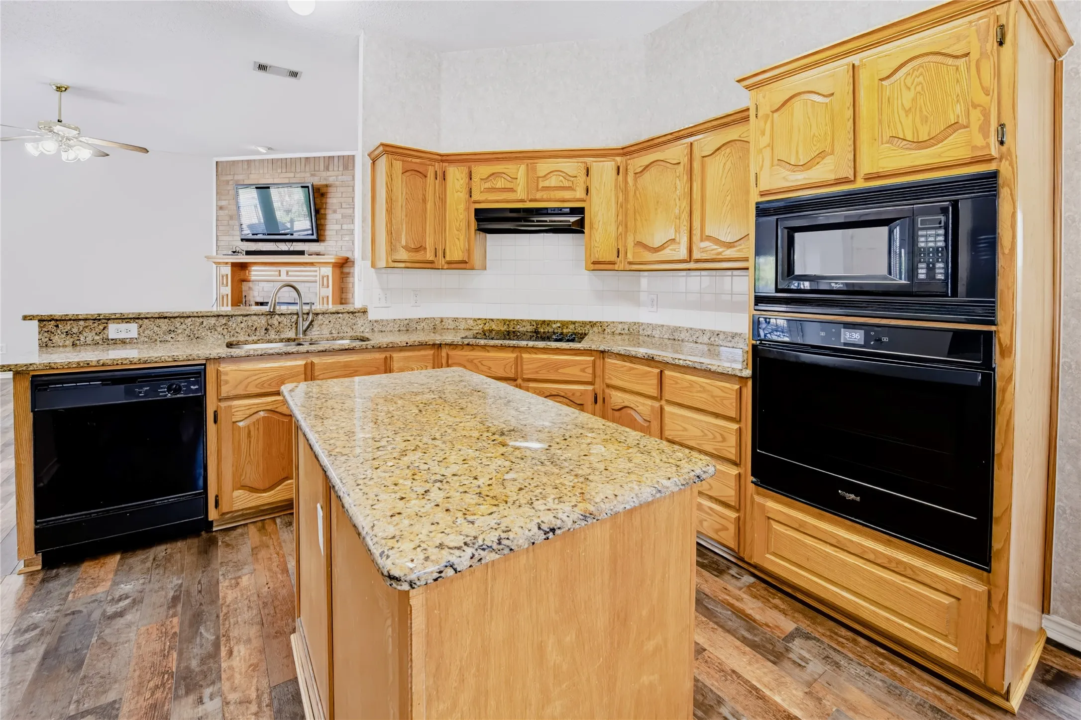 Kitchen featuring wood cabinetry, stone-surface countertops, central island, and black built-in appliances including a wall oven and microwave