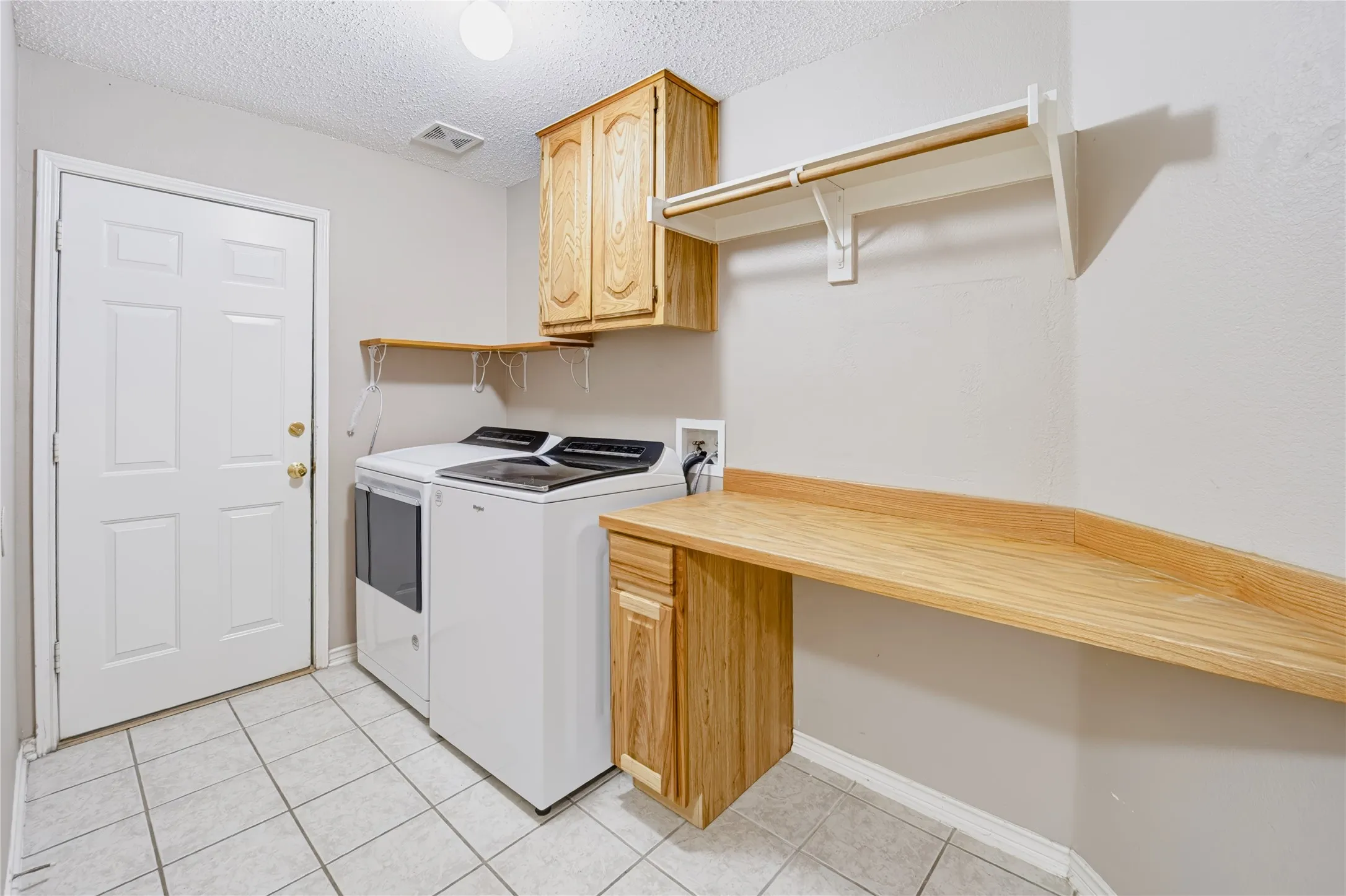 Laundry area featuring ceramic tile flooring, wood-finish cabinetry, a dedicated workspace with a wood-surface counter, and overhead shelving