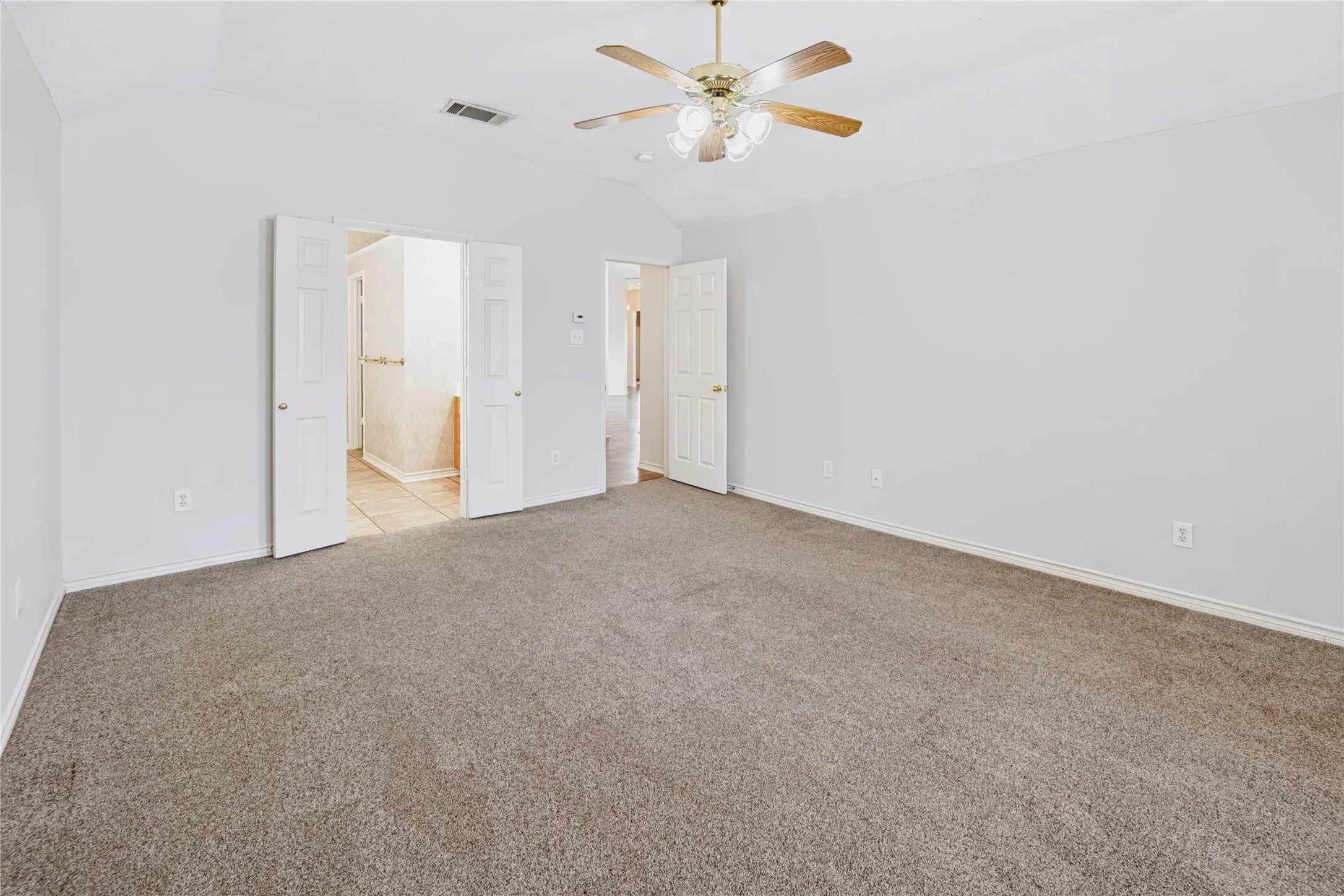 Vaulted ceiling featuring a central multi-blade ceiling fan with integrated lighting, neutral wall finishes, and carpeting