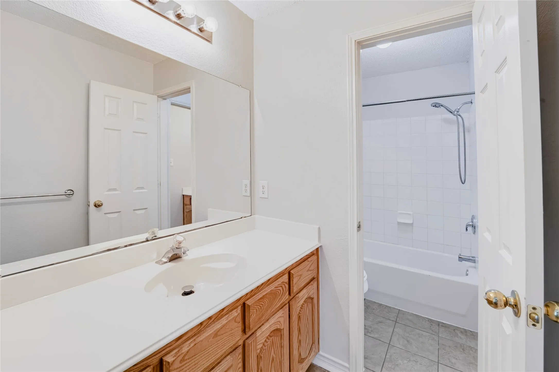 Bathroom vanity featuring a solid-surface countertop, integrated sink, wood-finish cabinetry, a full-width wall mirror, and a tub-shower combination with white wall tile