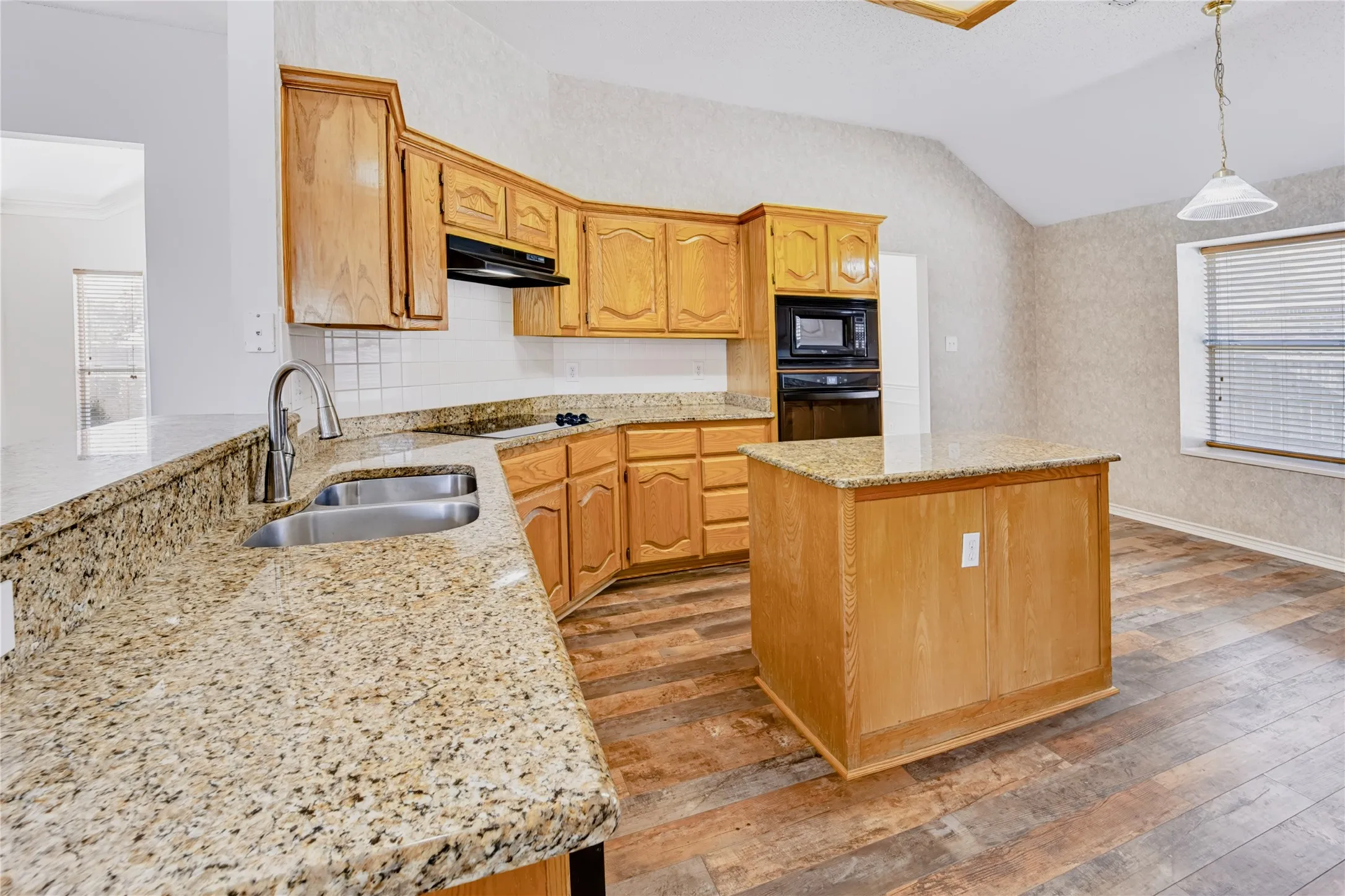 Kitchen featuring wood cabinetry, stone countertops, a center island, built-in appliances, and wood-finish flooring under a vaulted ceiling