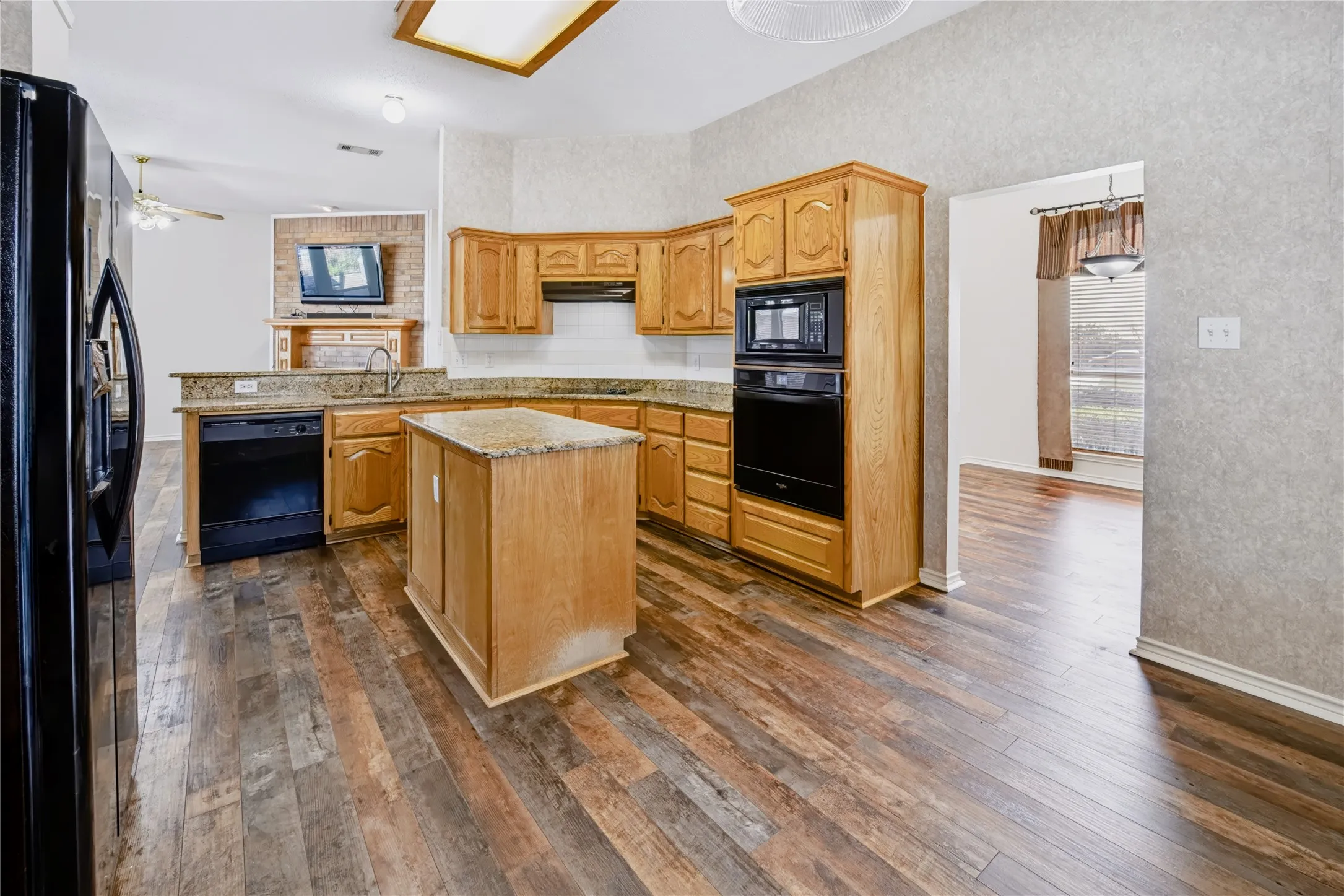 Kitchen featuring medium-tone wood cabinetry, stone countertops, central island, wood-finish flooring, and built-in black wall oven and microwave