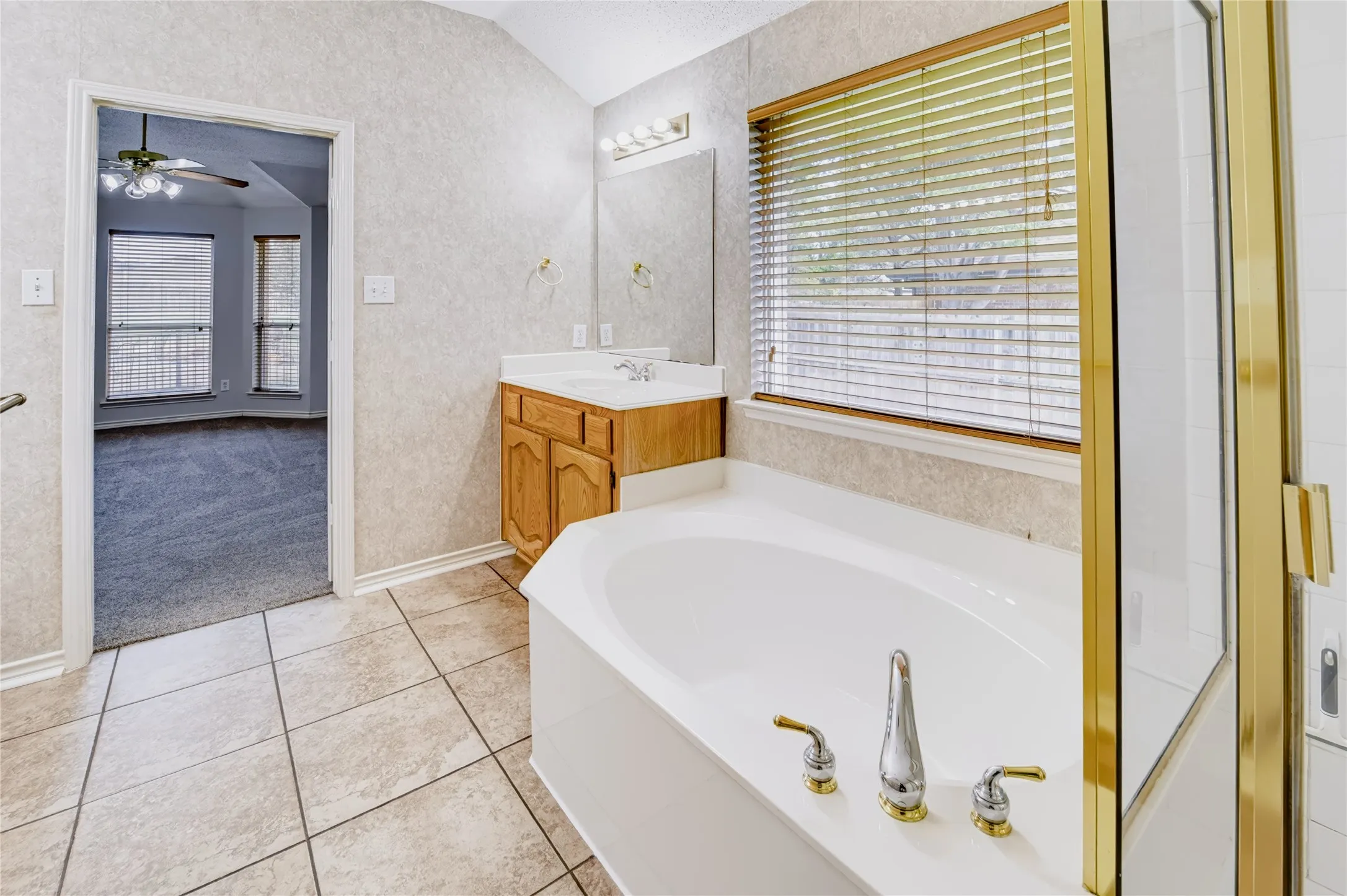 Bathroom featuring tile flooring, a built-in soaking tub with deck-mounted faucet, wood-finish vanity with countertop, and a glass-enclosed shower