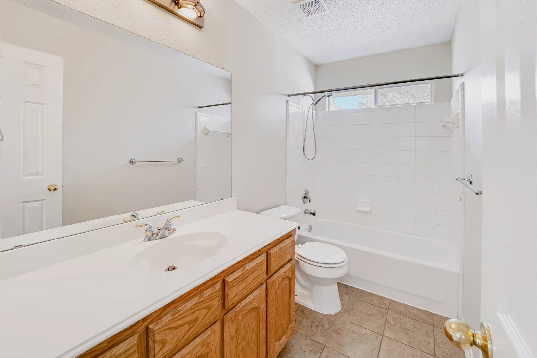 Bathroom featuring a vanity with a white solid-surface countertop, an oversized wall-mounted mirror, ceramic tile flooring, and a tub-shower combination with full-height white wall tiling