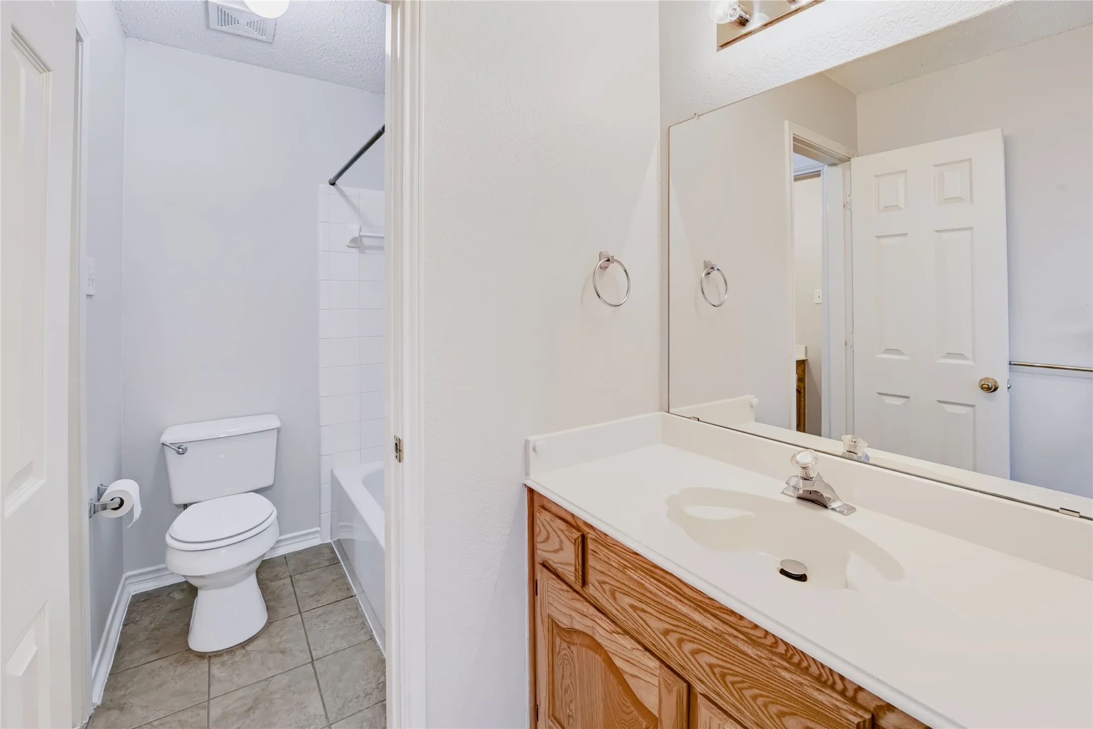 Bathroom featuring a wood-finish vanity with a white countertop, large wall-mounted mirror, ceramic tile flooring, and a shower-tub combination with white tile surround