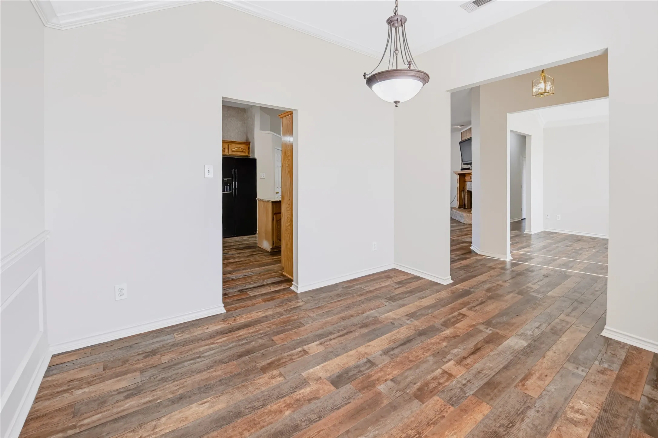 Interior featuring wood-finish flooring, crown molding, chair rail trim, and a hanging pendant light fixture