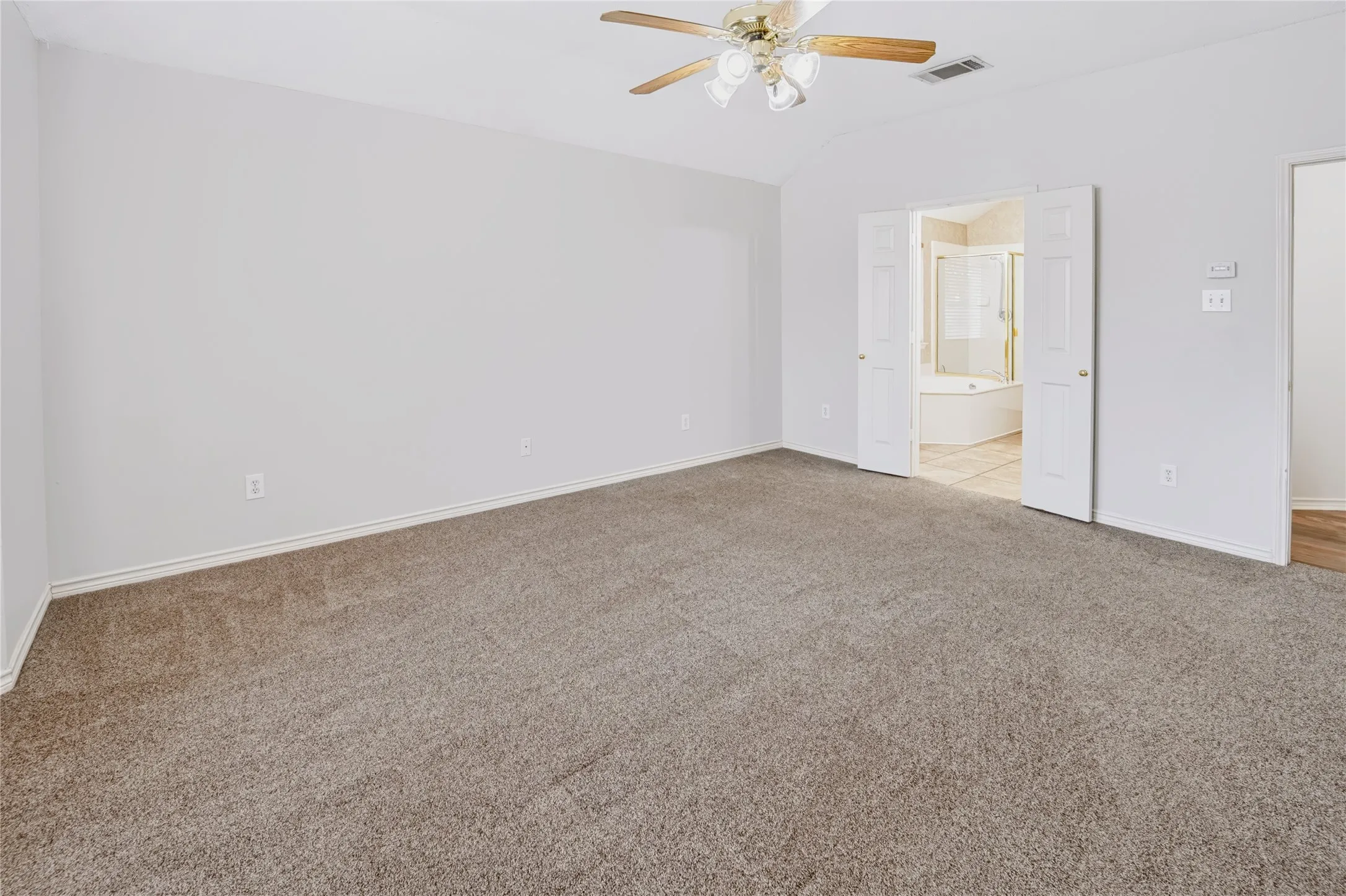 Spacious room featuring neutral carpeting, a vaulted ceiling, and a ceiling fan with integrated lighting