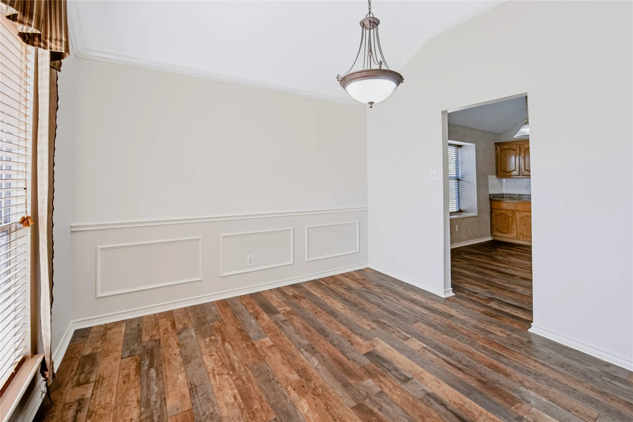 Room featuring wood-finish flooring, wainscoting, vaulted ceiling, and an architectural pendant light fixture