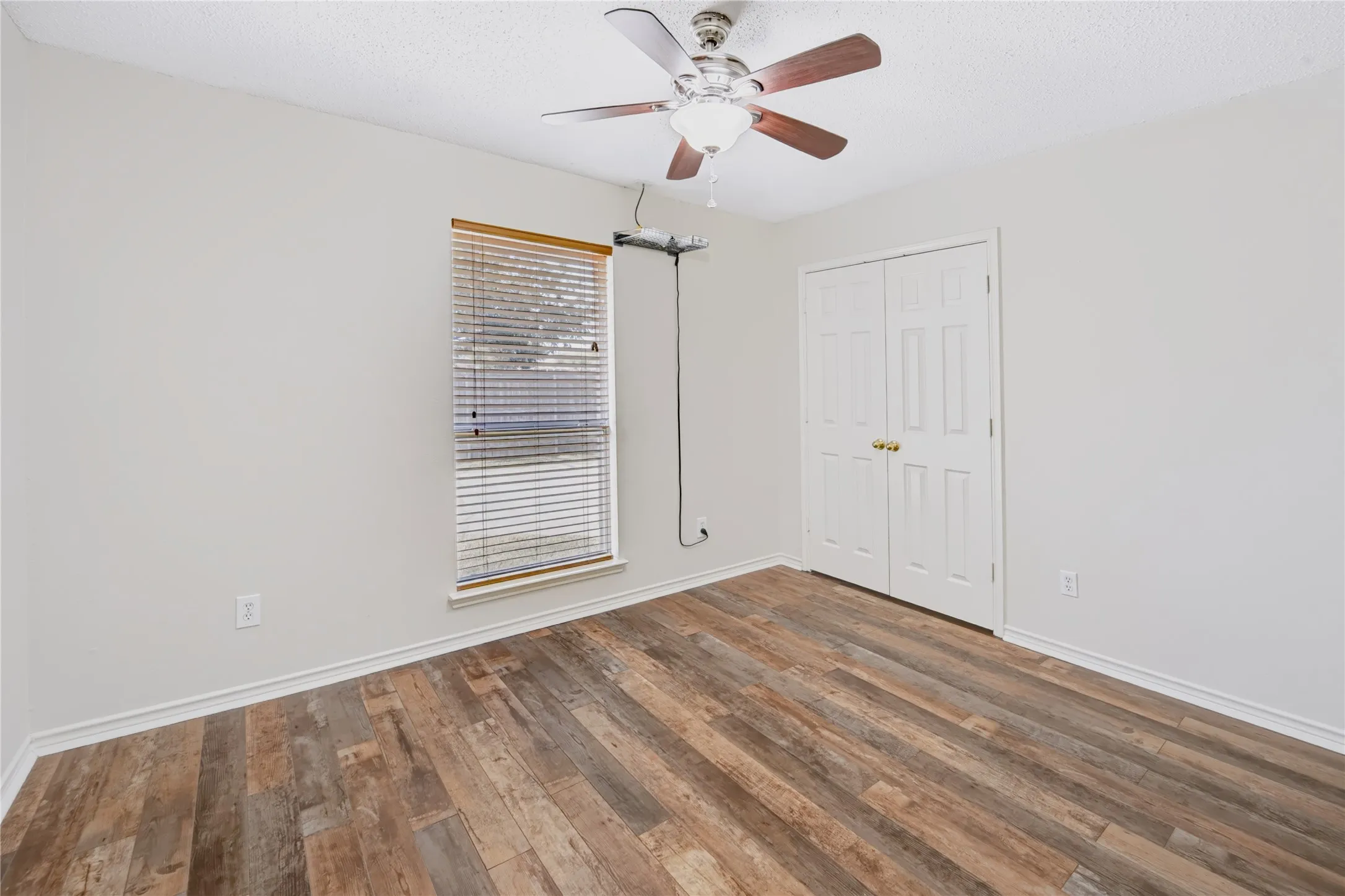 Wood-finish flooring, multi-paneled closet doors, ceiling fan with integrated light fixture, and horizontal window blinds