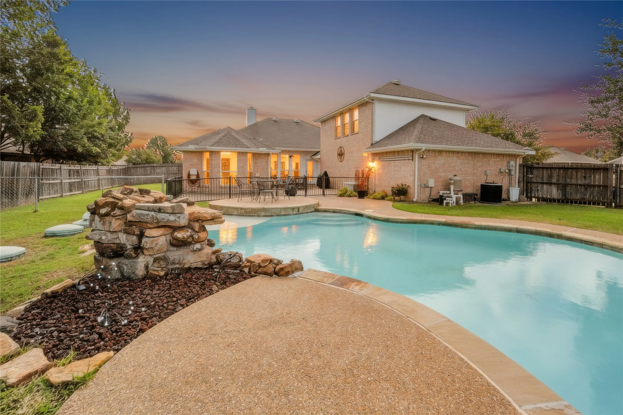 Backyard featuring a swimming pool with a stone rock feature, concrete decking, grass lawn, and wood privacy fencing