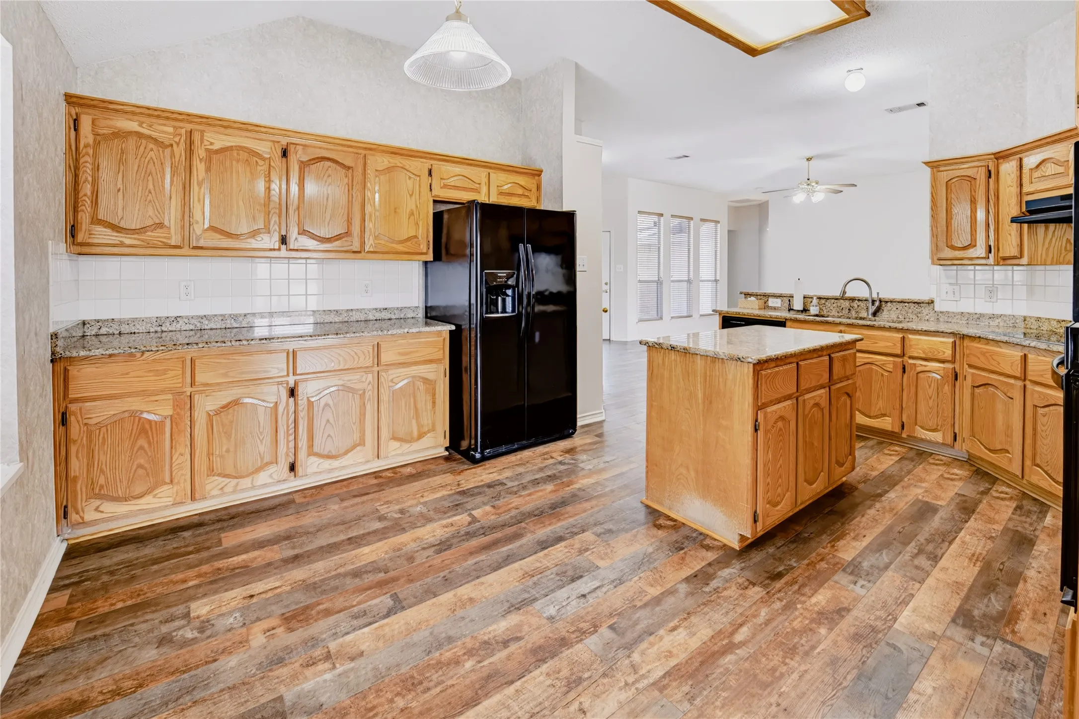 Kitchen featuring wood-finish cabinetry, stone countertops, central island, wood-finish flooring, and subway tile backsplash