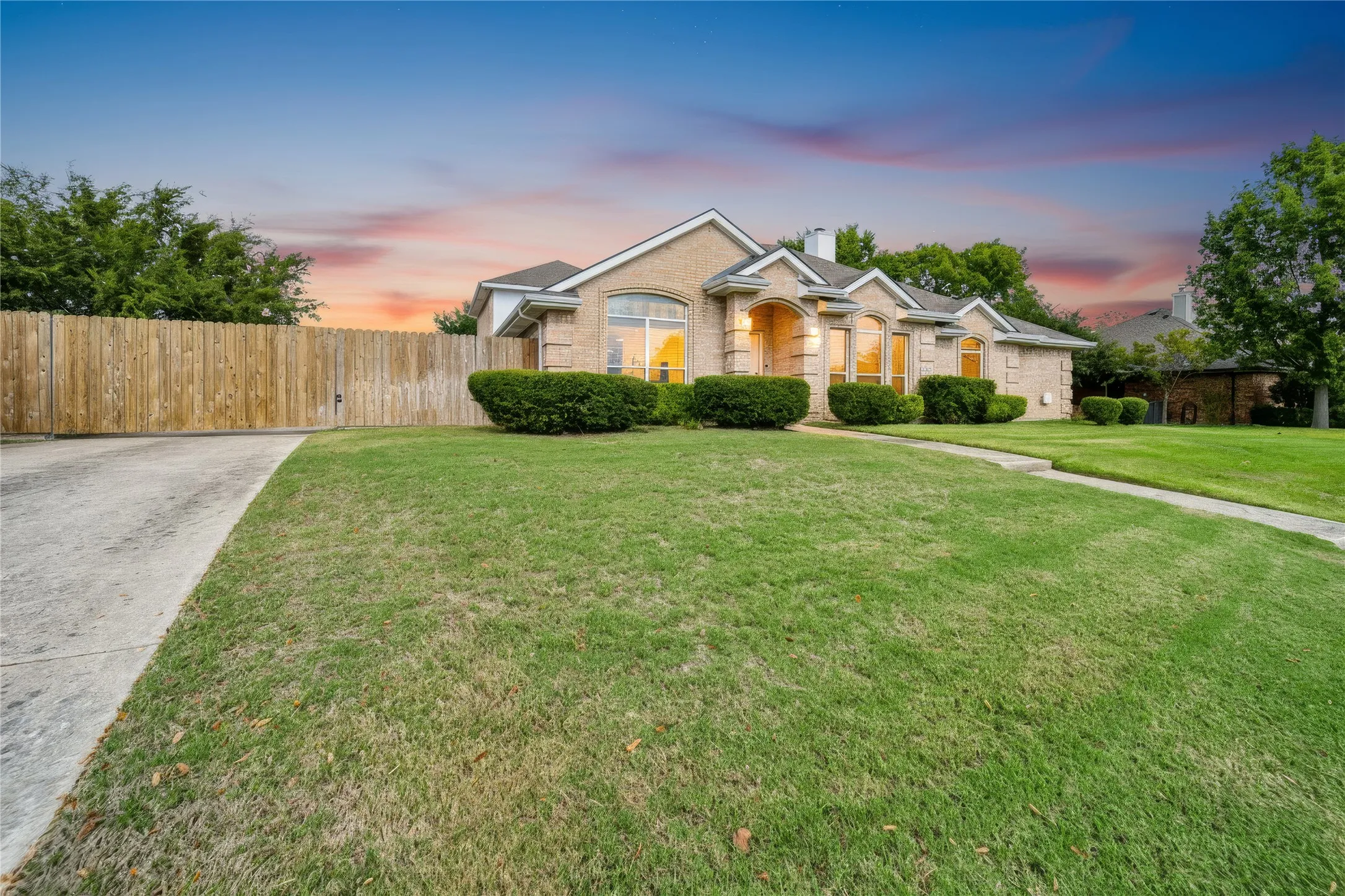 Single-story brick exterior featuring an arched entryway, decorative stone window headers, a concrete driveway, and a wooden privacy fence