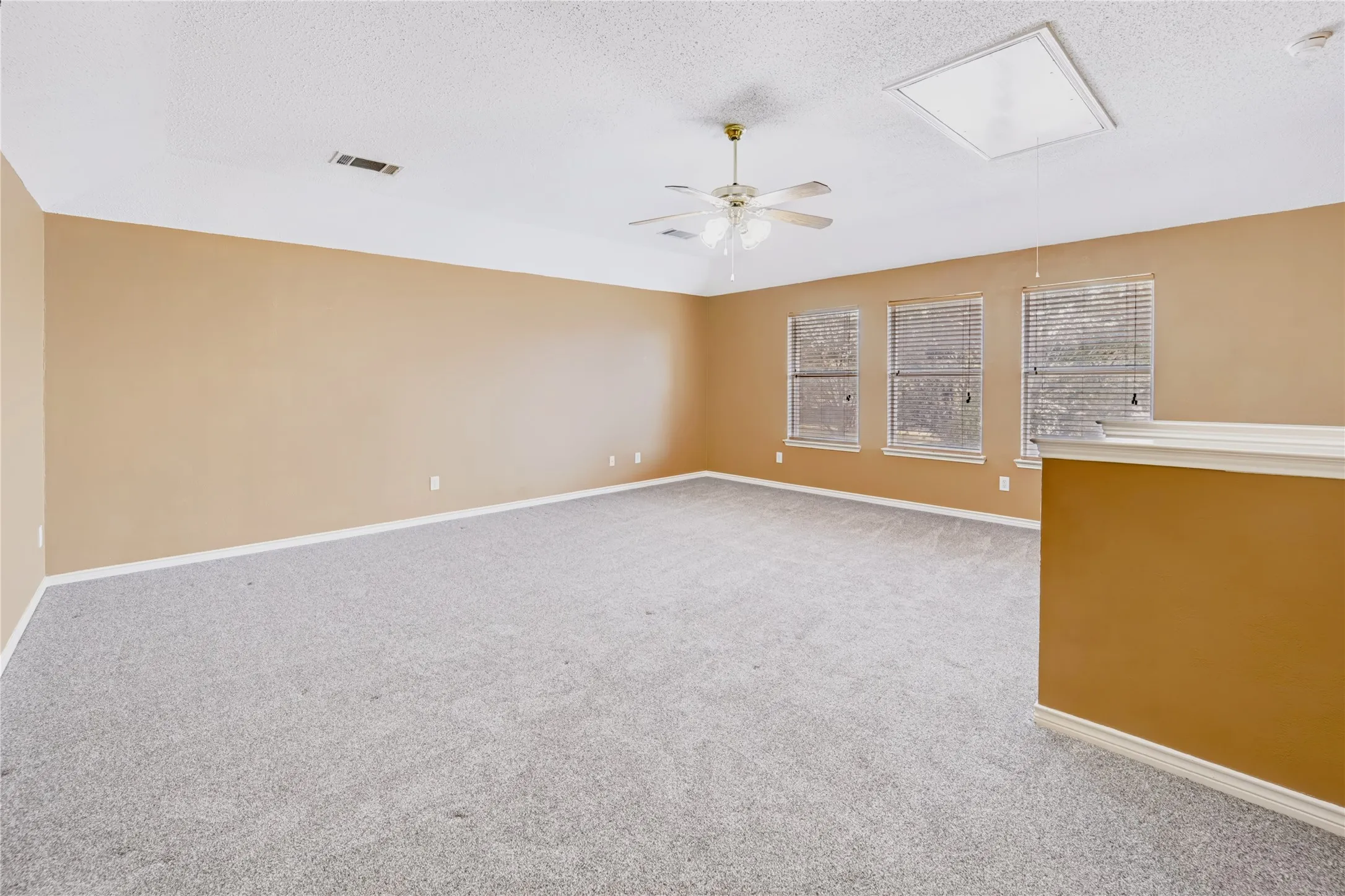 Expansive room featuring a tray ceiling, wall-to-wall carpeting, a ceiling fan with integrated lighting, and multiple windows