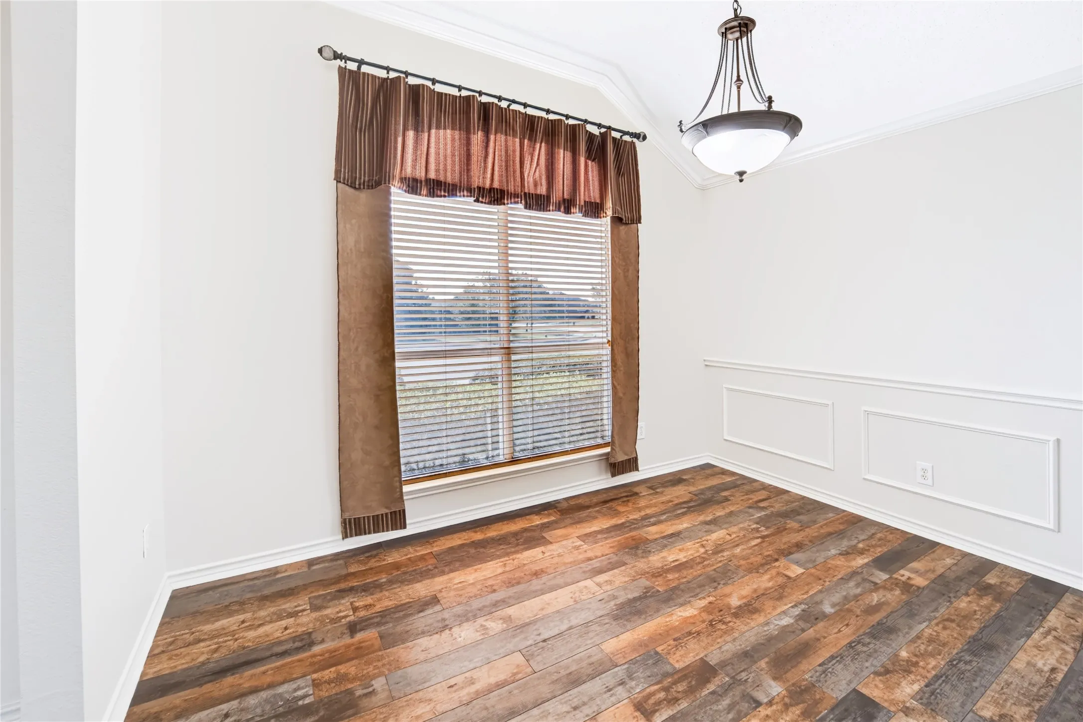 Vaulted ceiling featuring a multi-light chandelier, wood-finish flooring, and lower-wall picture frame wainscoting