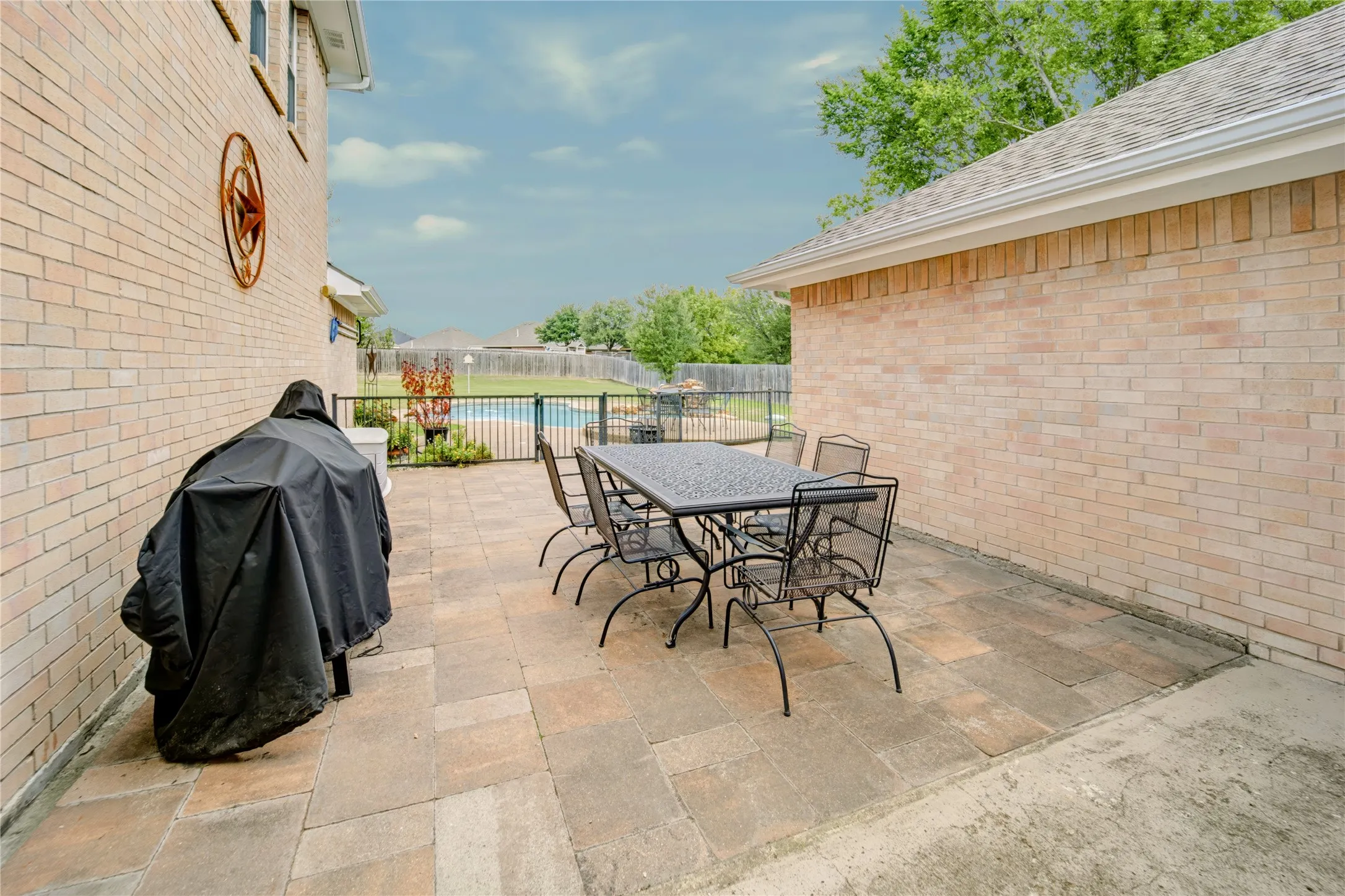 Exterior brick patio featuring paver stone flooring, enclosed swimming pool area, and metal perimeter fencing
